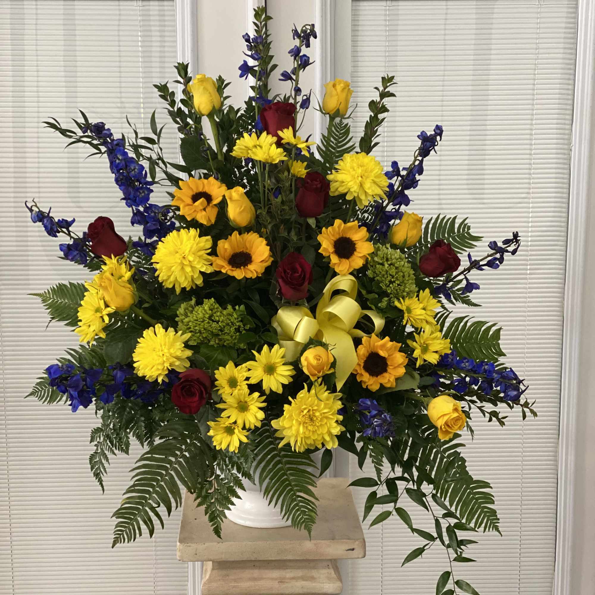 Large mixed flower arrangement in a white vase with yellow, red, and blue blooms