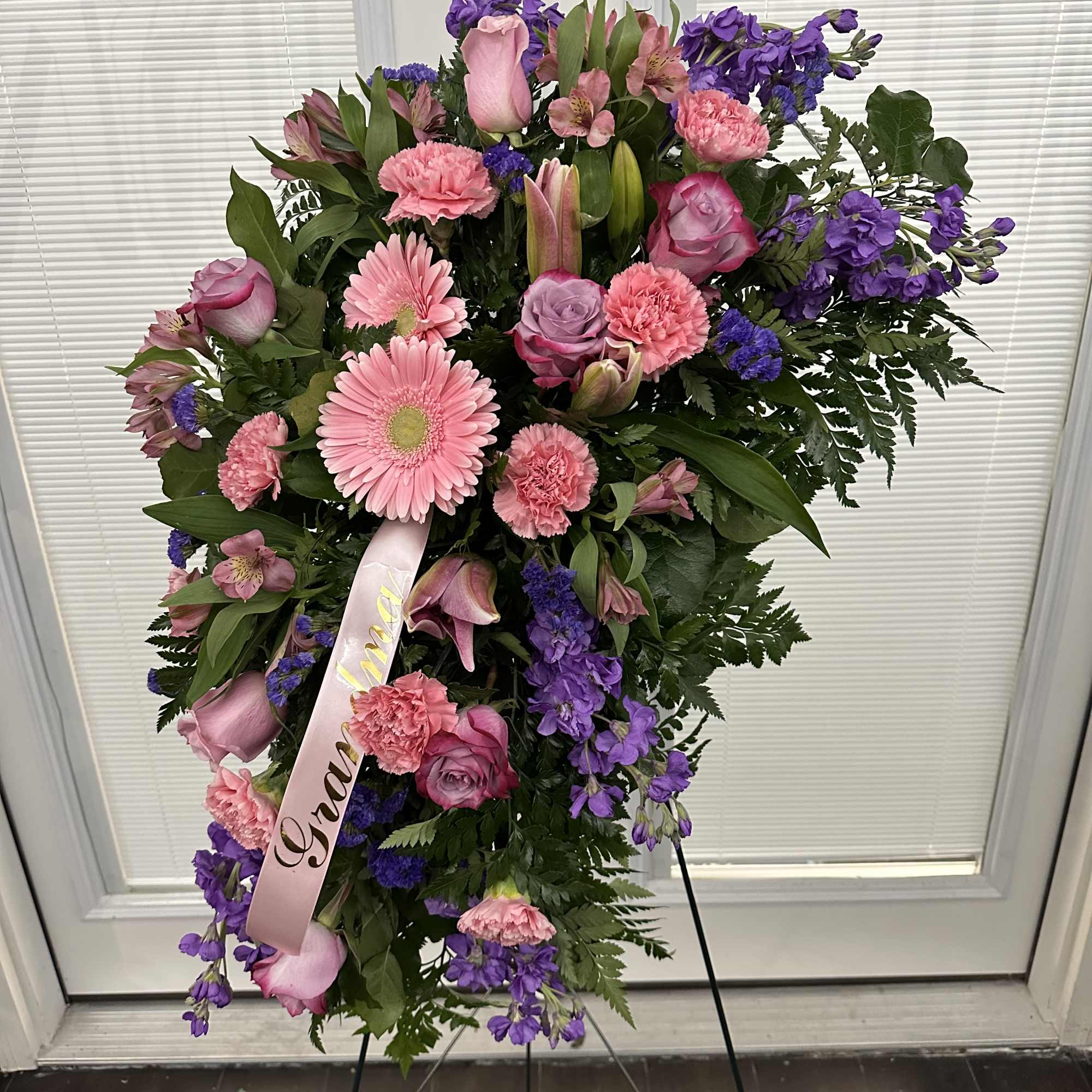 Standing spray of pink and purple flowers on an easel with a ribbon