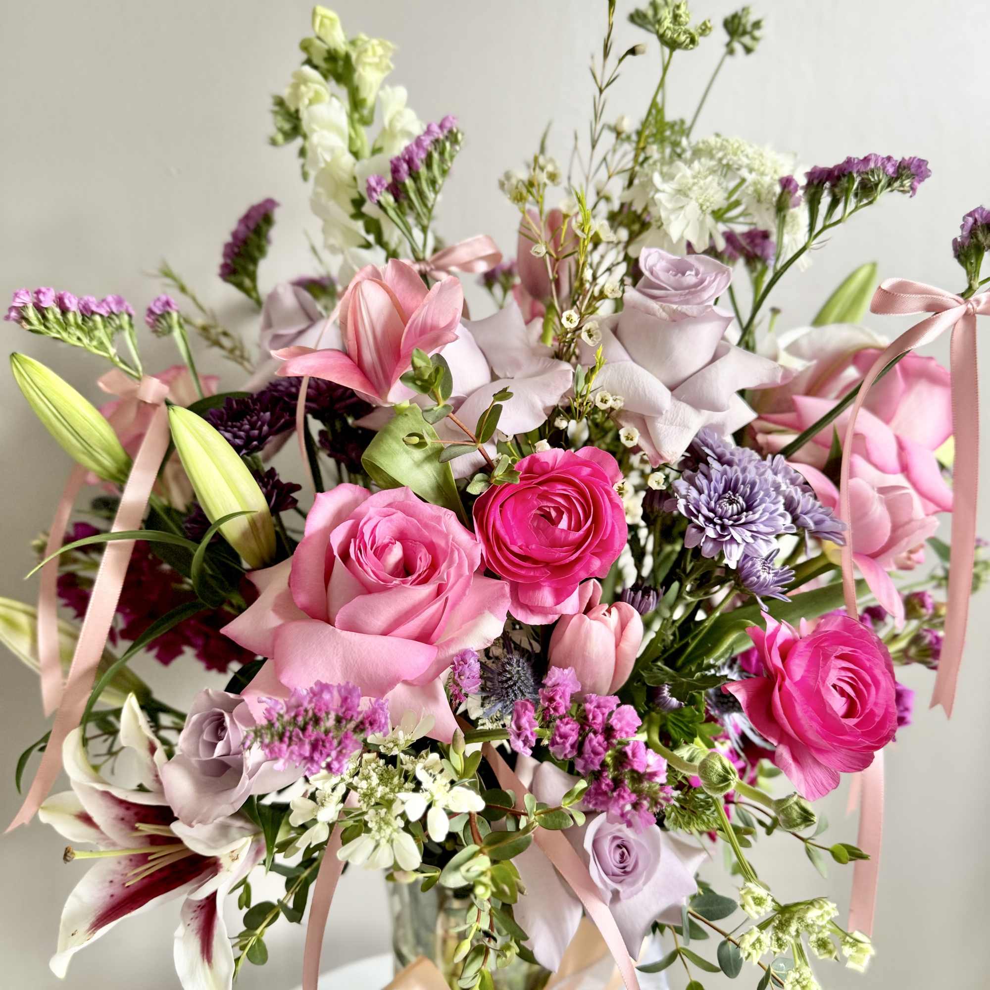 Bouquet of pink and lavender flowers in a glass vase with ribbon