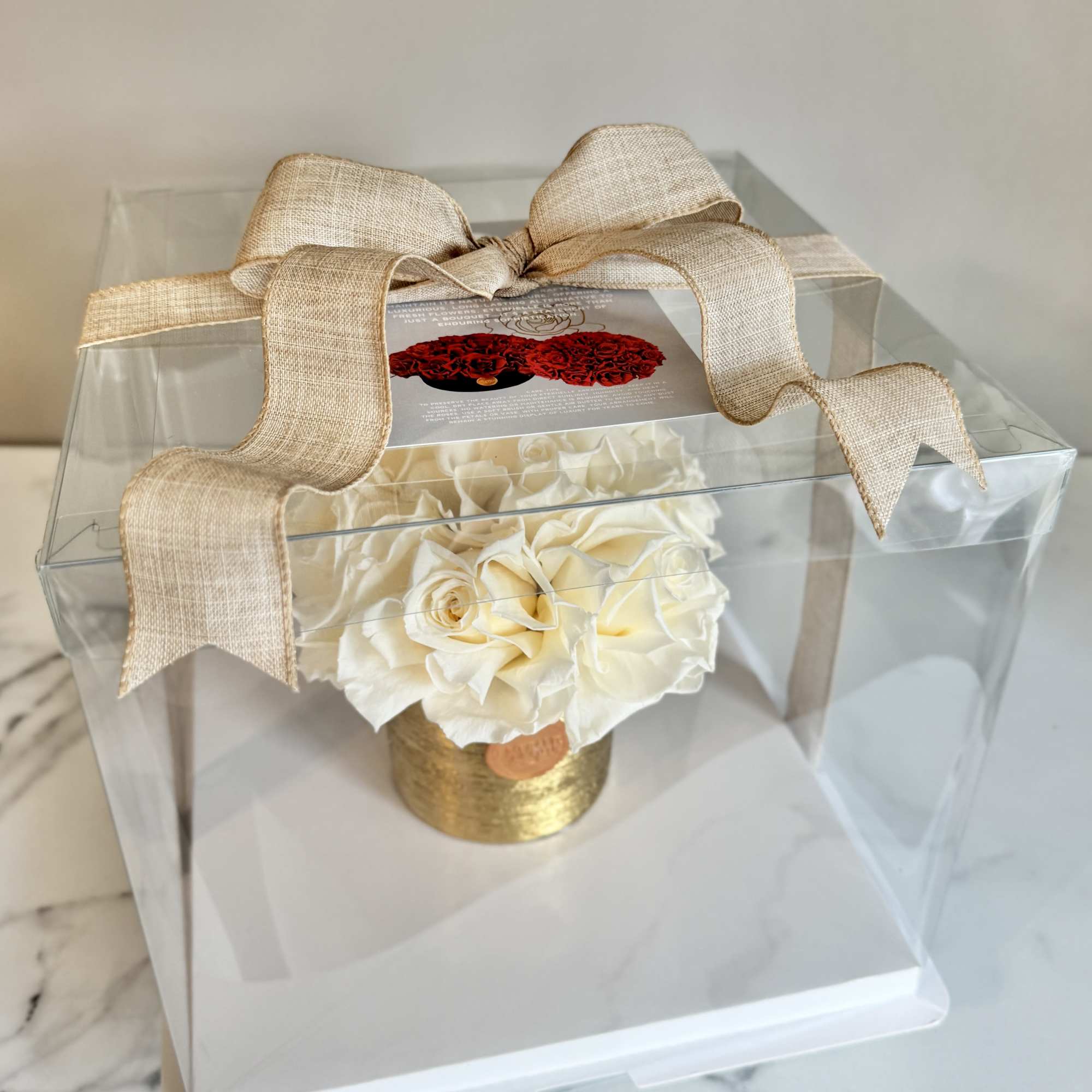 Cream rose arrangement in a clear gift box with a beige ribbon