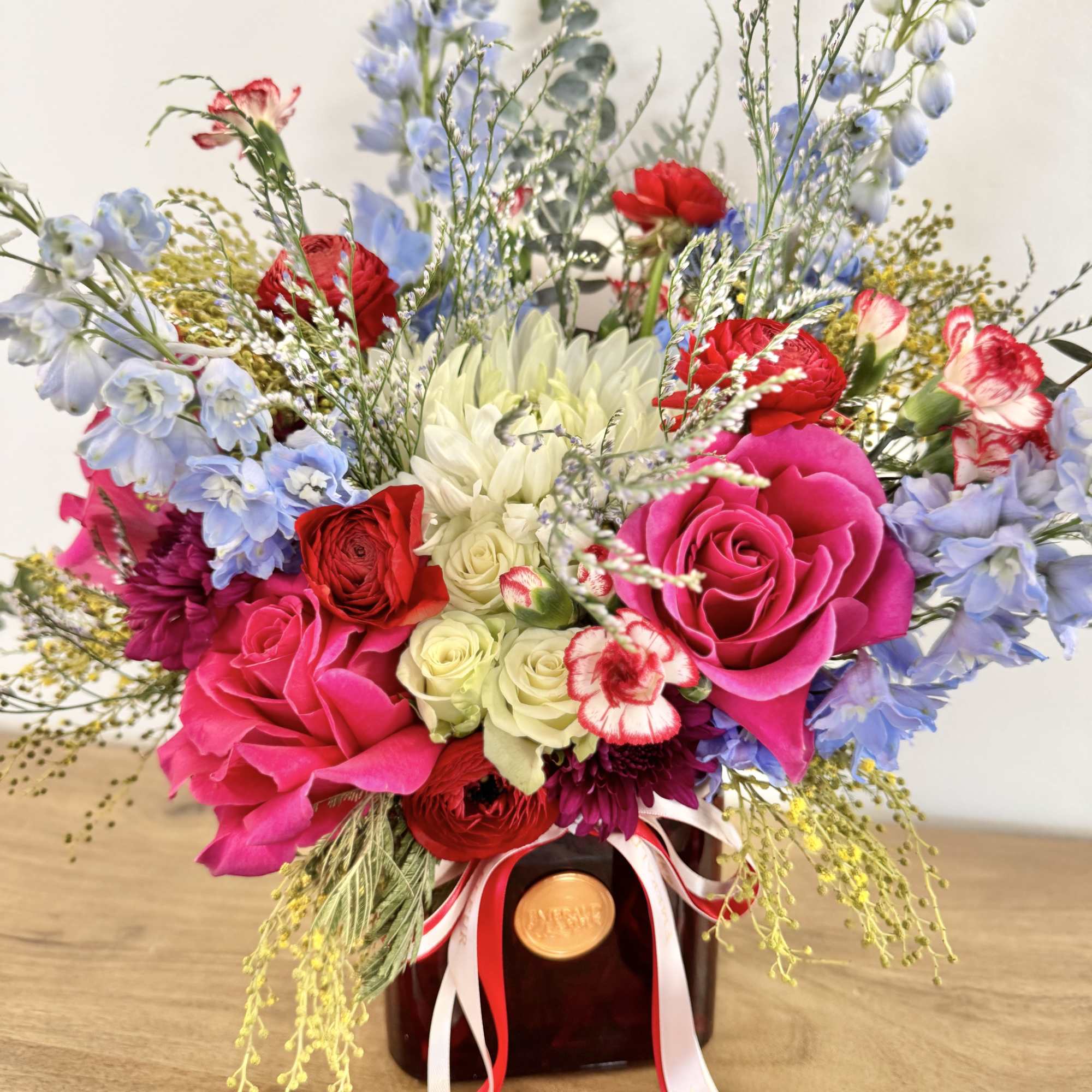 Mixed bouquet of pink, red, white, and blue flowers in a dark vase