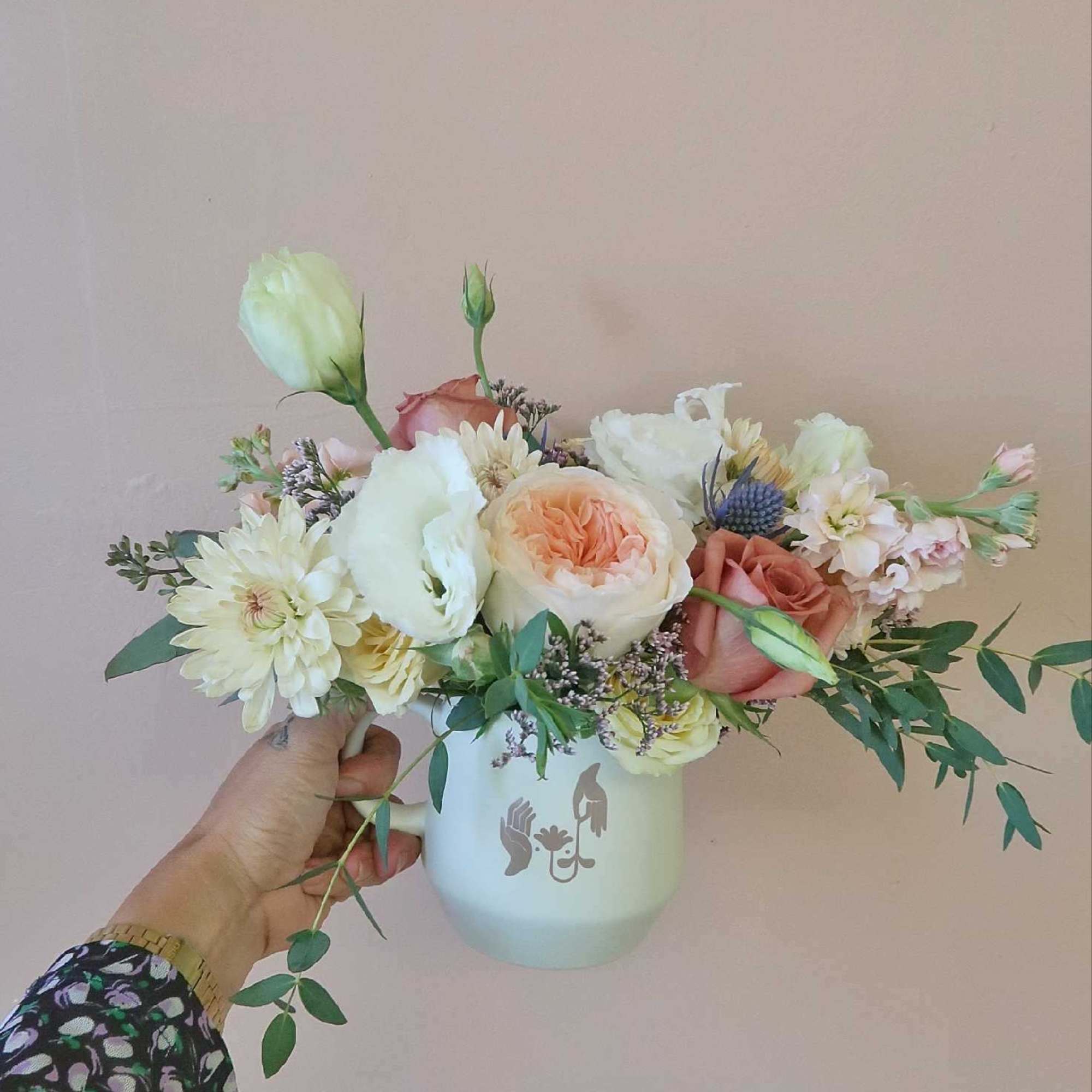 Handheld bouquet of pastel roses and white blooms in a white mug vase