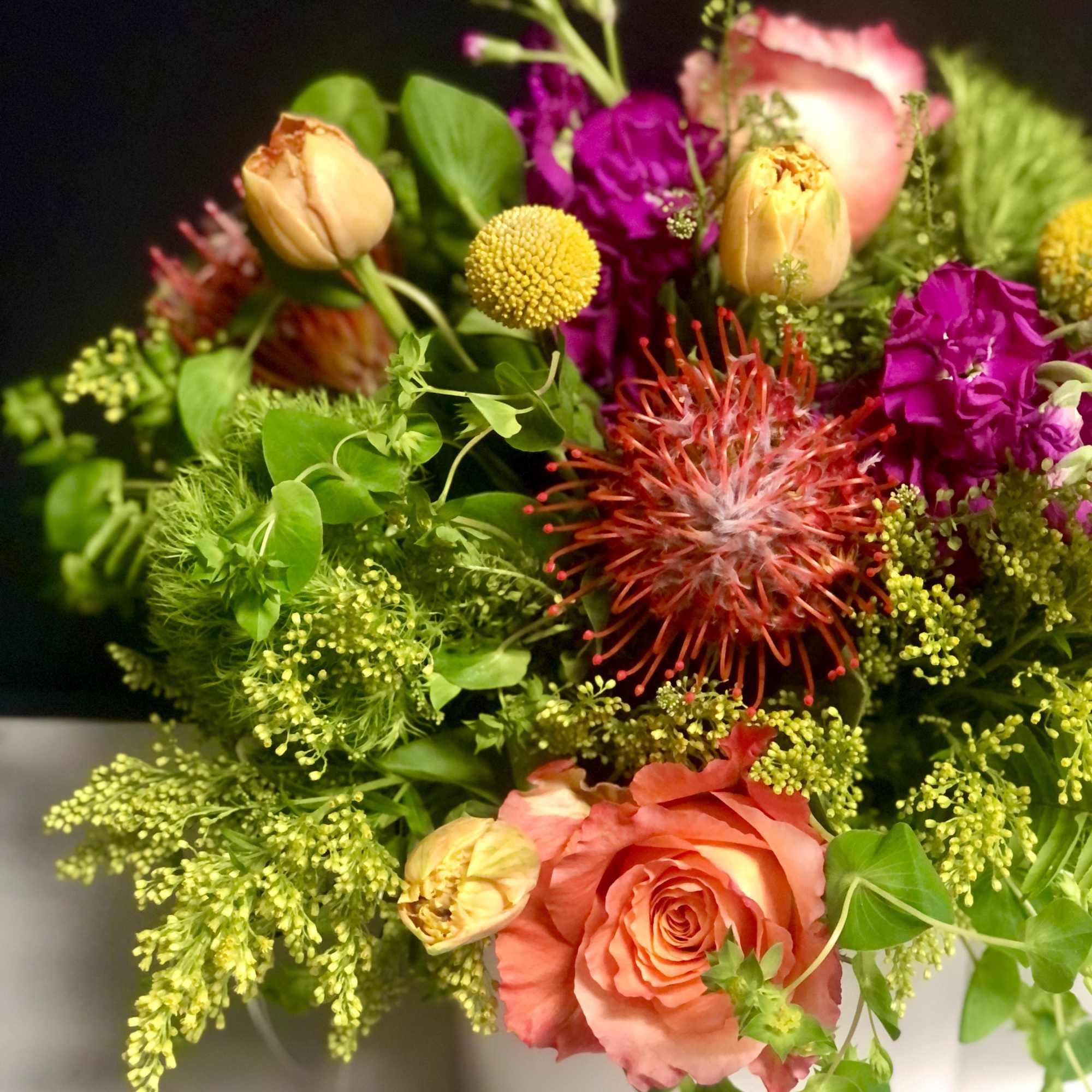 Mixed bouquet of coral roses, tulips, and bright accent flowers in a white vase
