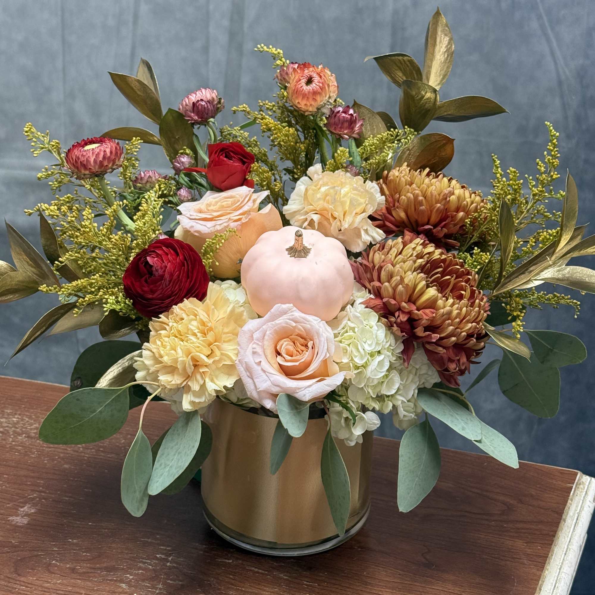 Mixed bouquet in a gold vase with roses, chrysanthemums, and a small pumpkin