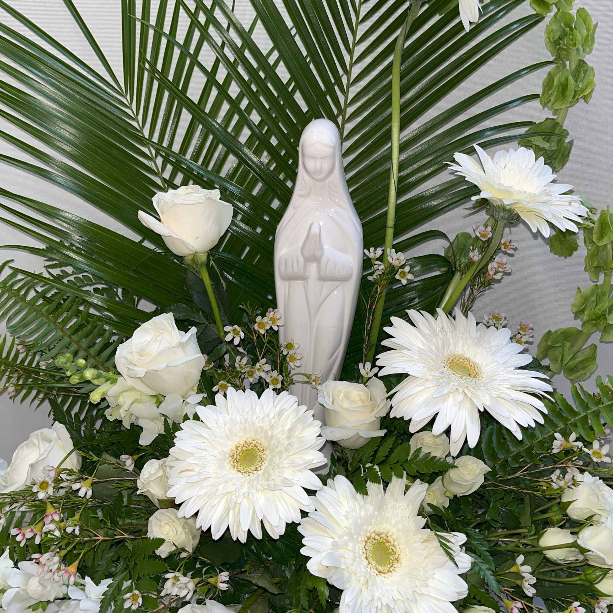 White floral arrangement with a ceramic Virgin Mary statue