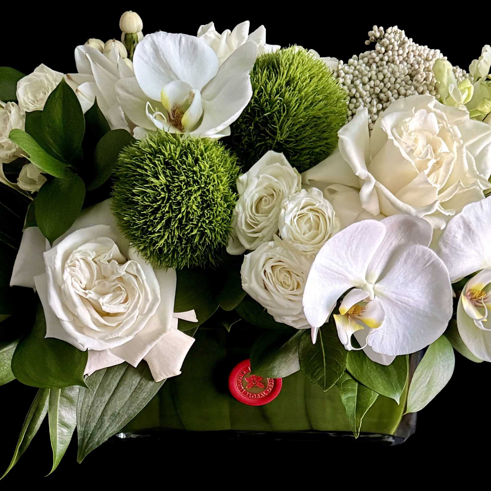 White floral arrangement with orchids and roses in a low container