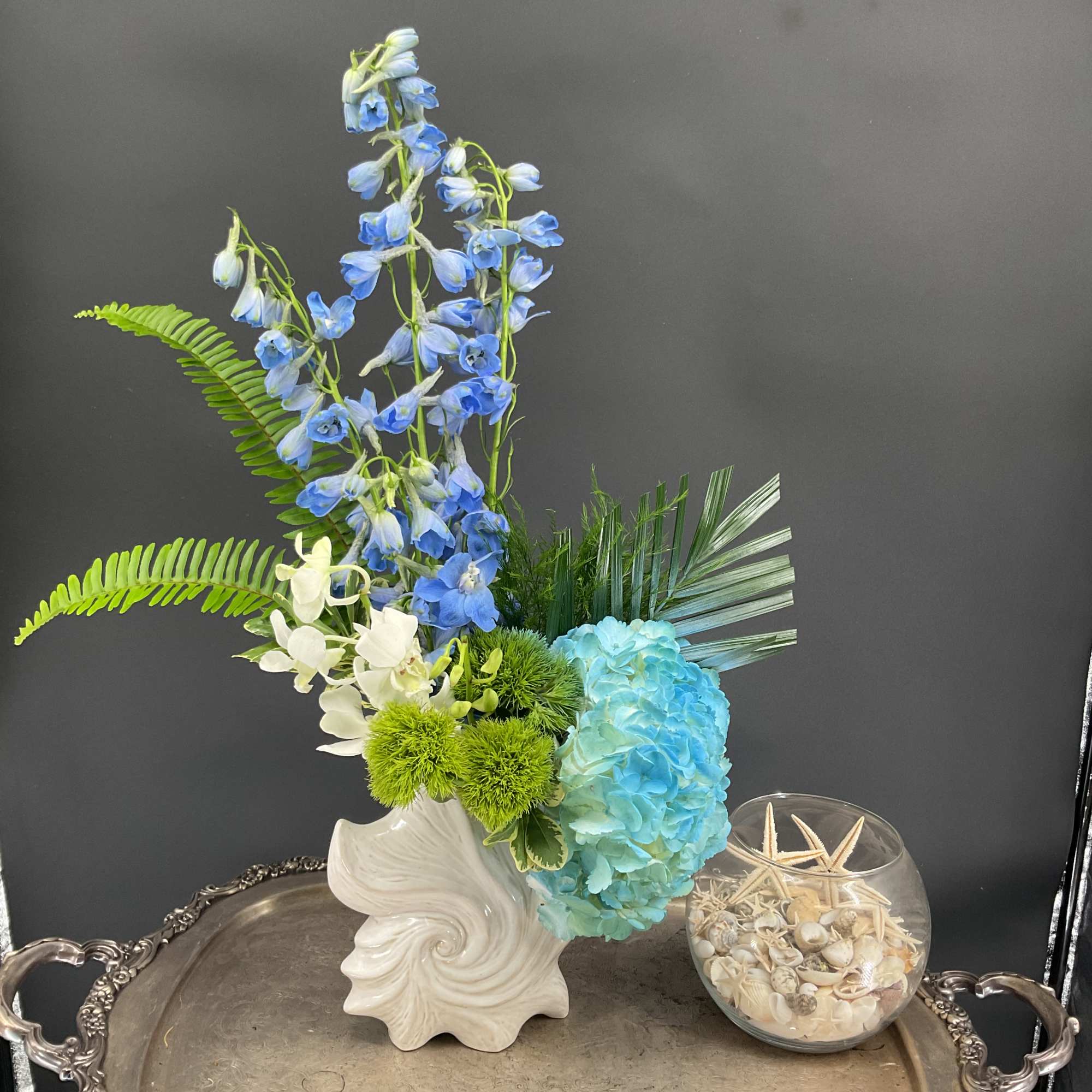 Blue and white floral arrangement in a white vase with green accents