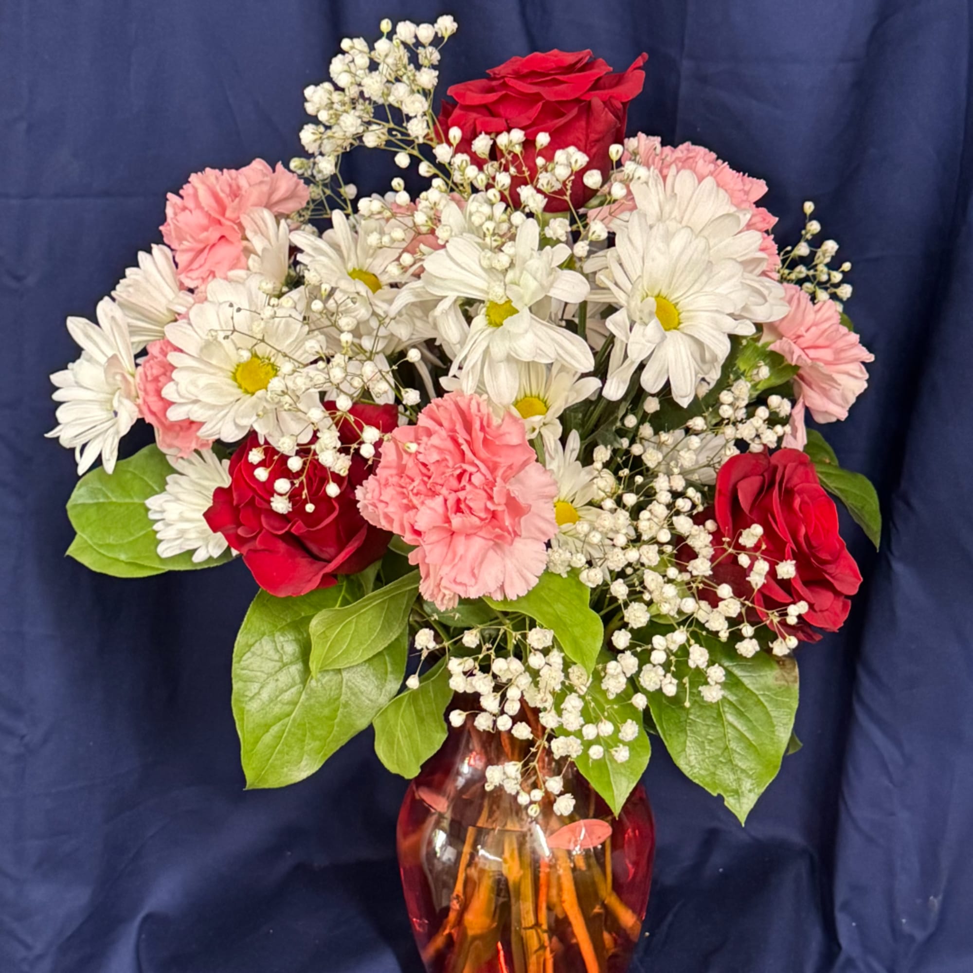 Bouquet of red roses, white daisies, and pink carnations in a glass vase
