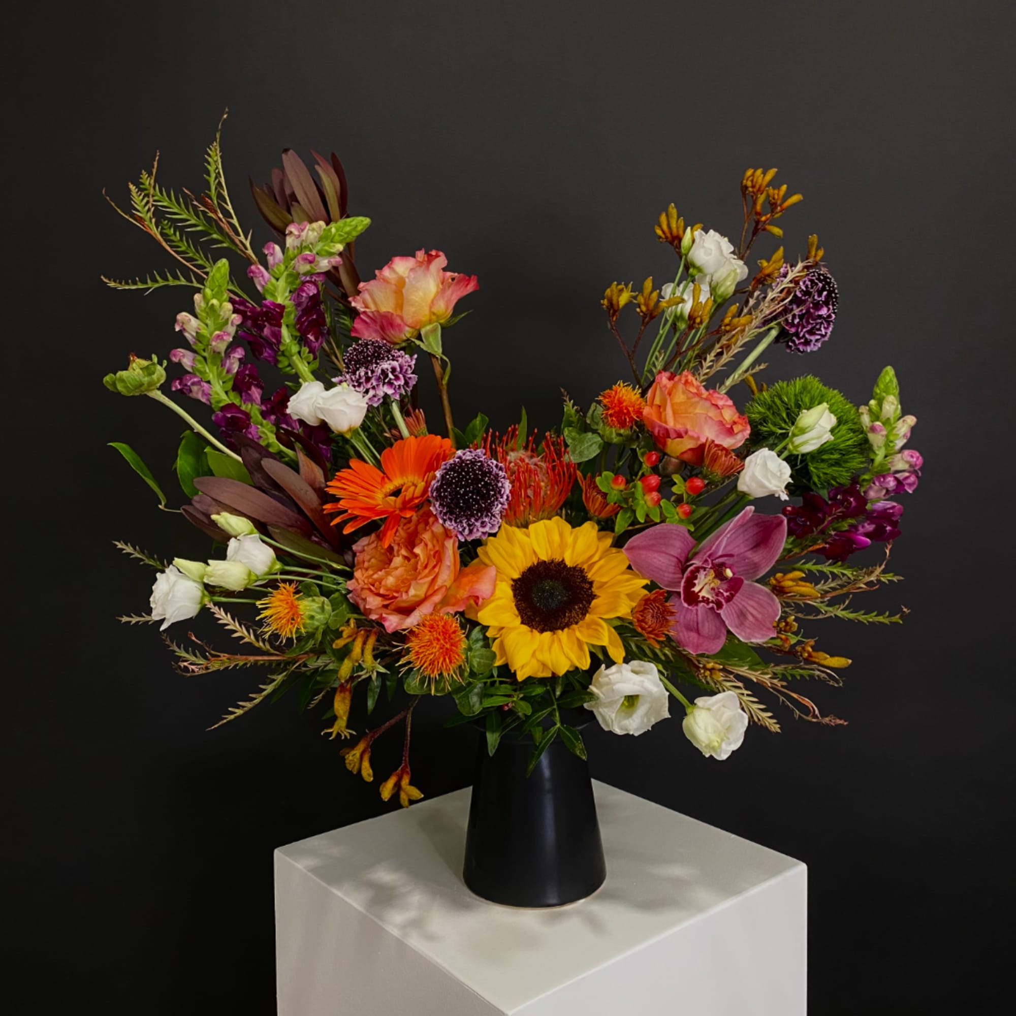 Colorful mixed bouquet in a black vase on a white pedestal