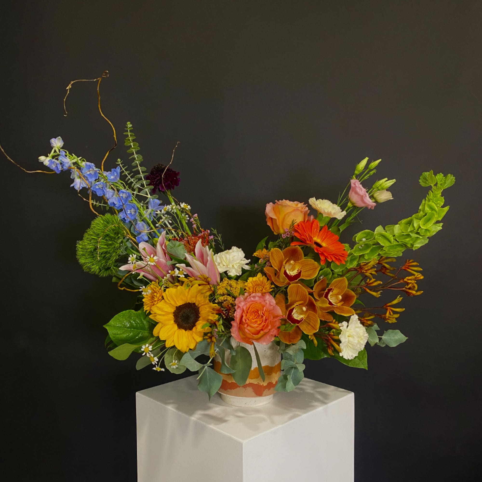 Colorful mixed flower arrangement in a patterned vase on a white pedestal