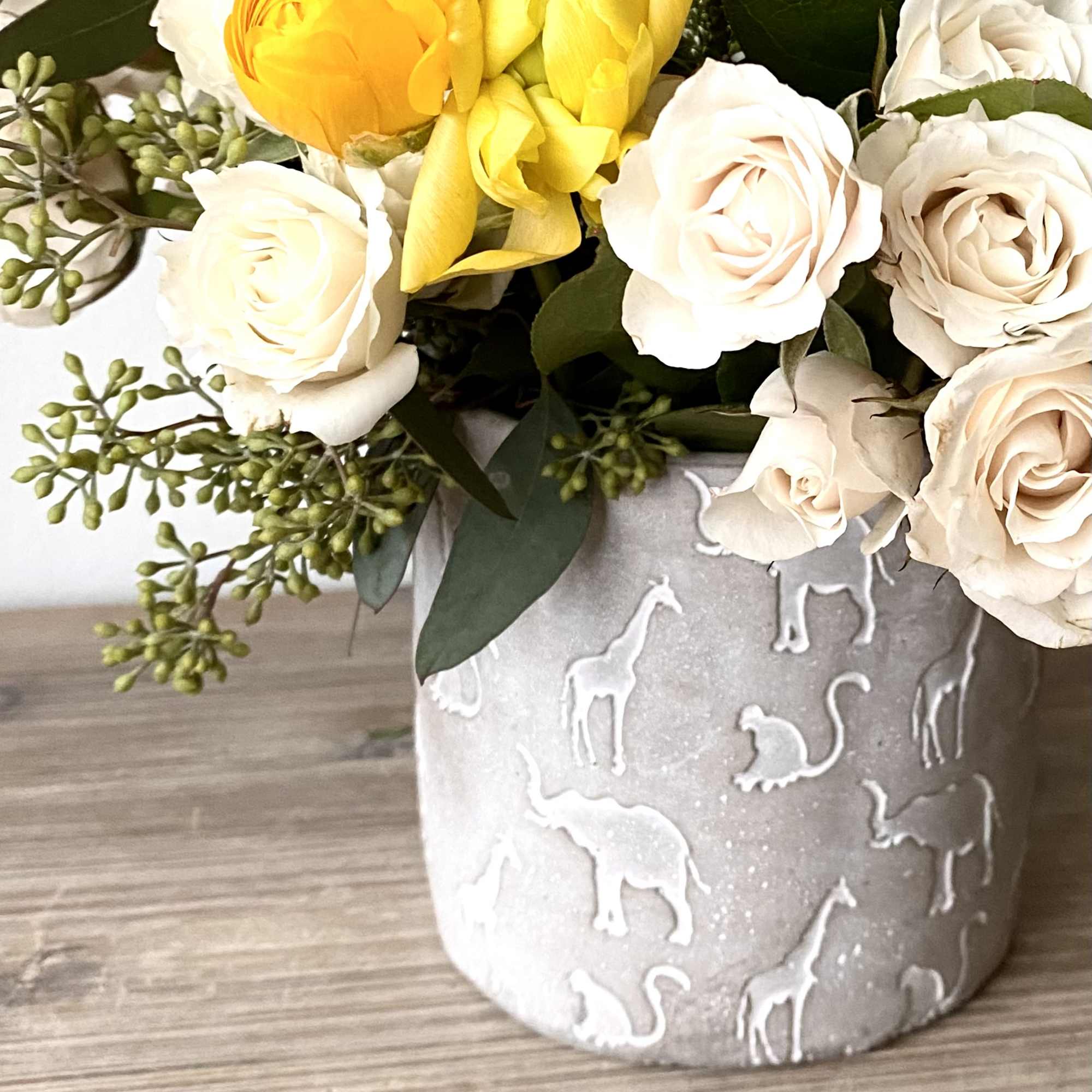 Yellow and white roses in a gray vase with animal reliefs