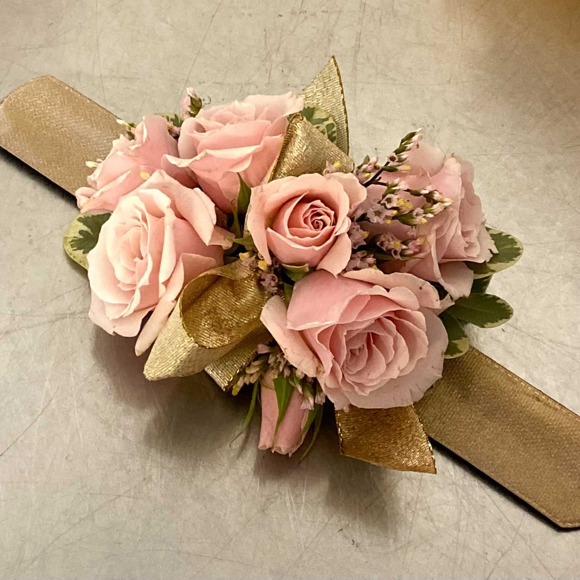 Pink rose corsage with gold ribbon on a neutral surface
