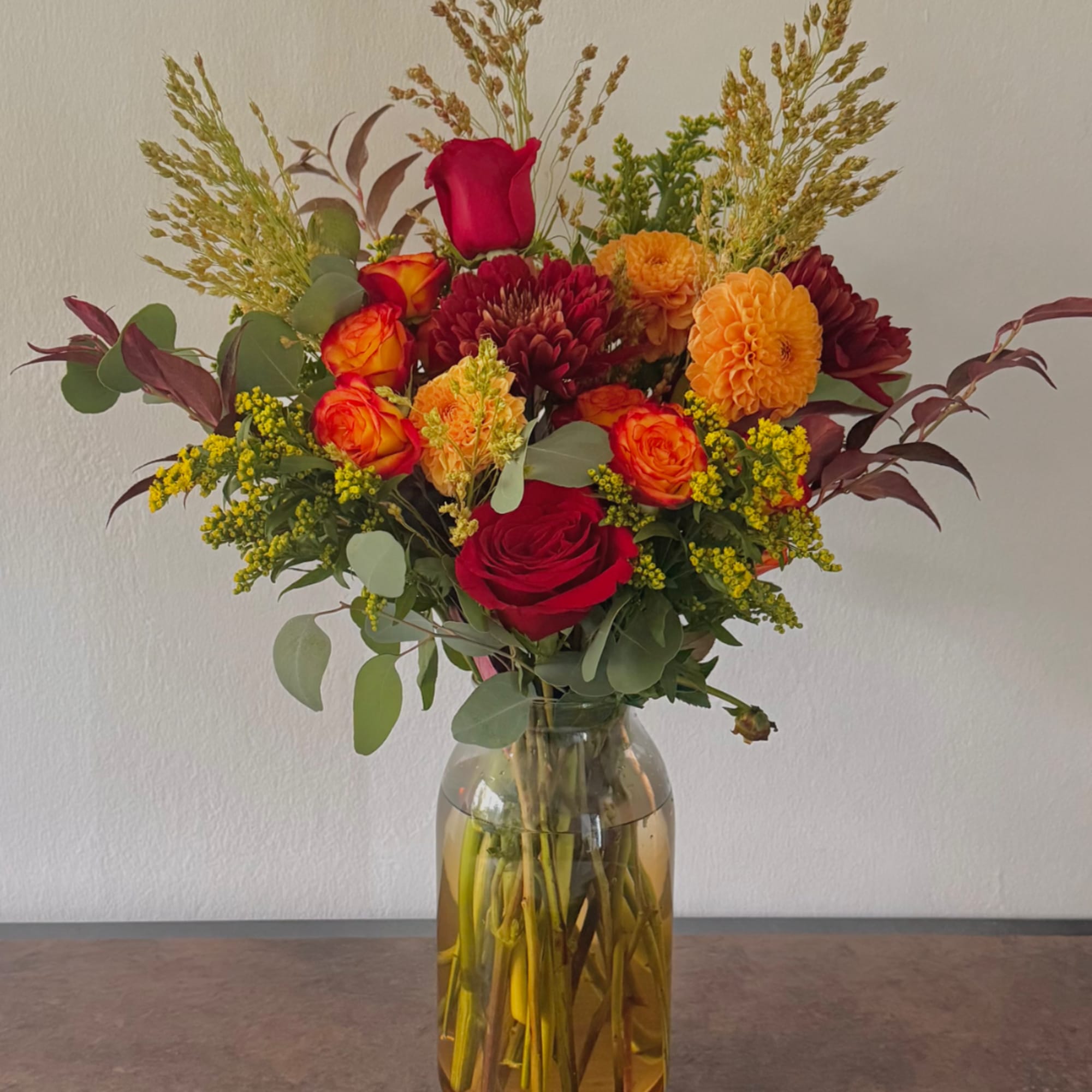 Mixed bouquet of red, orange, and yellow flowers in a glass vase