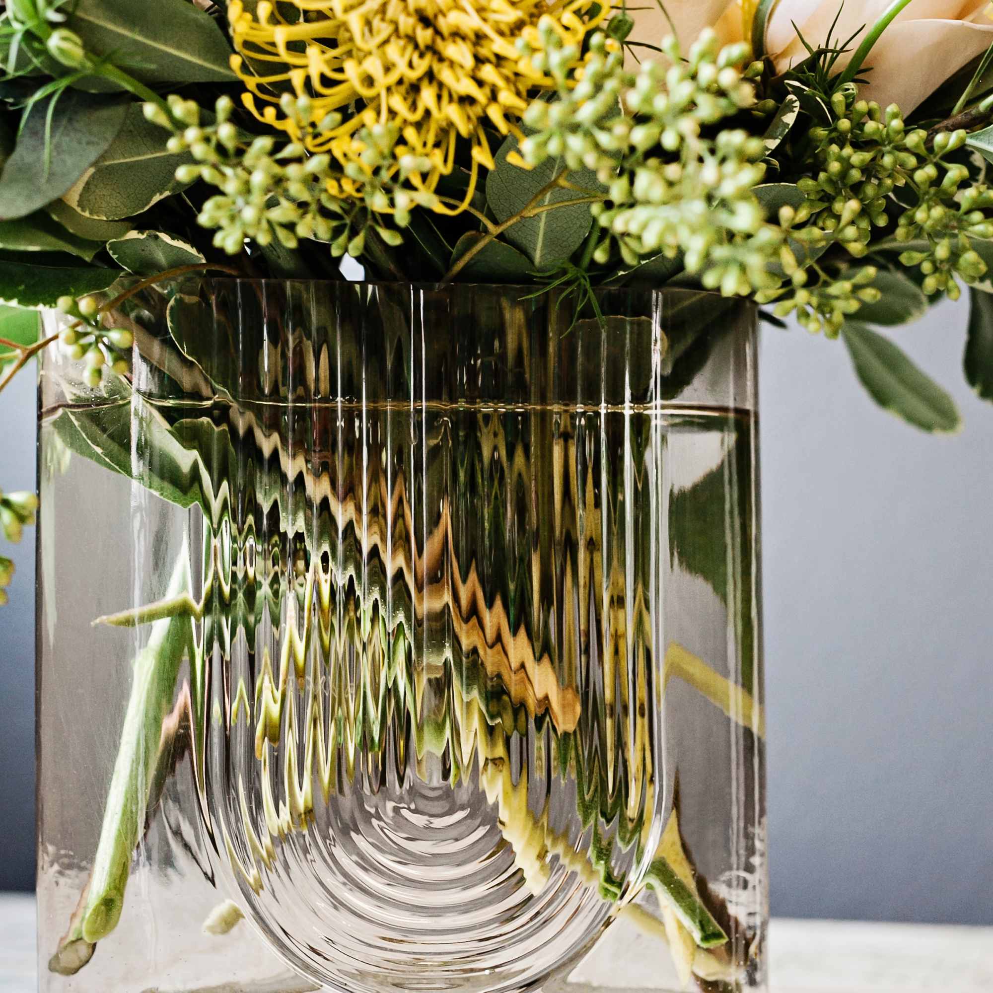 Yellow pincushion flower and pale roses in a clear glass vase