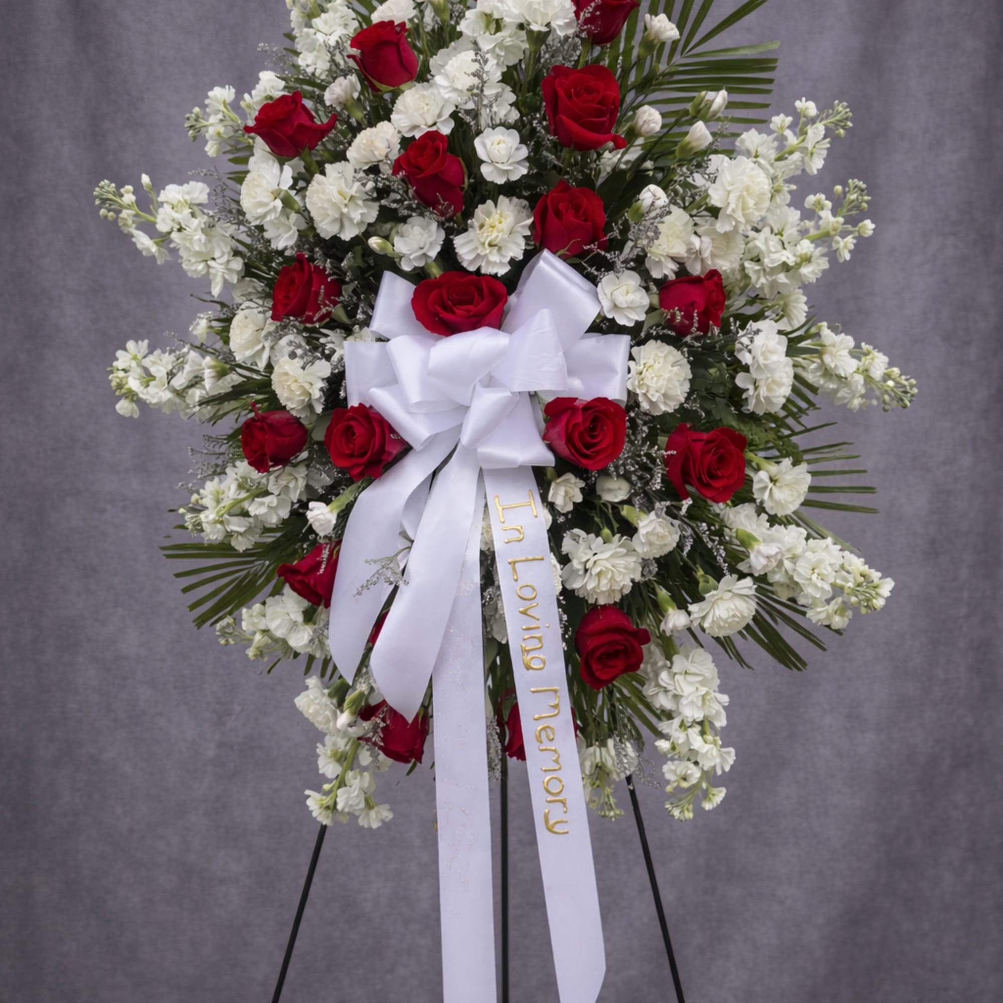 Standing red and white rose funeral spray with a white ribbon on an easel