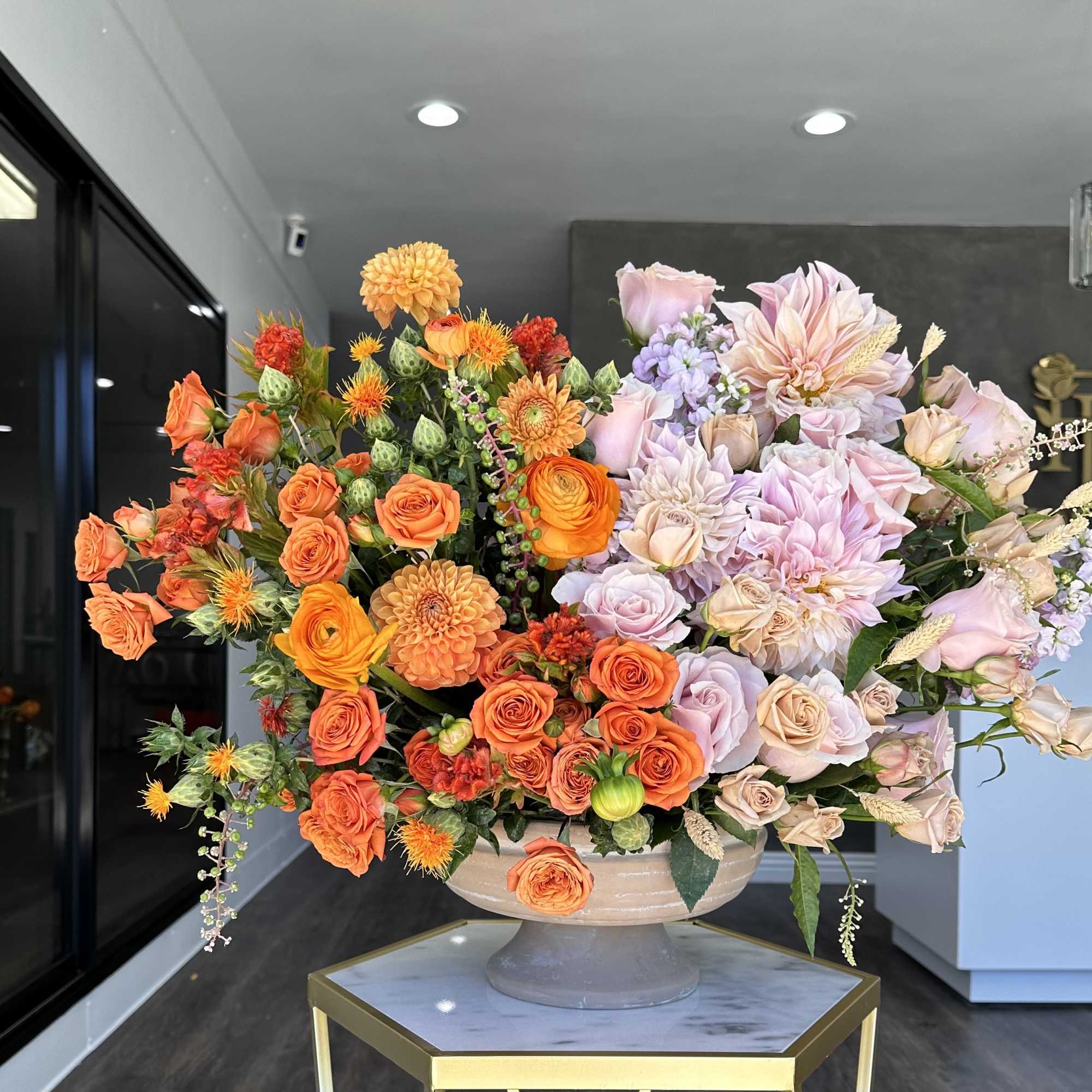 Large arrangement of orange and blush flowers in a pedestal bowl