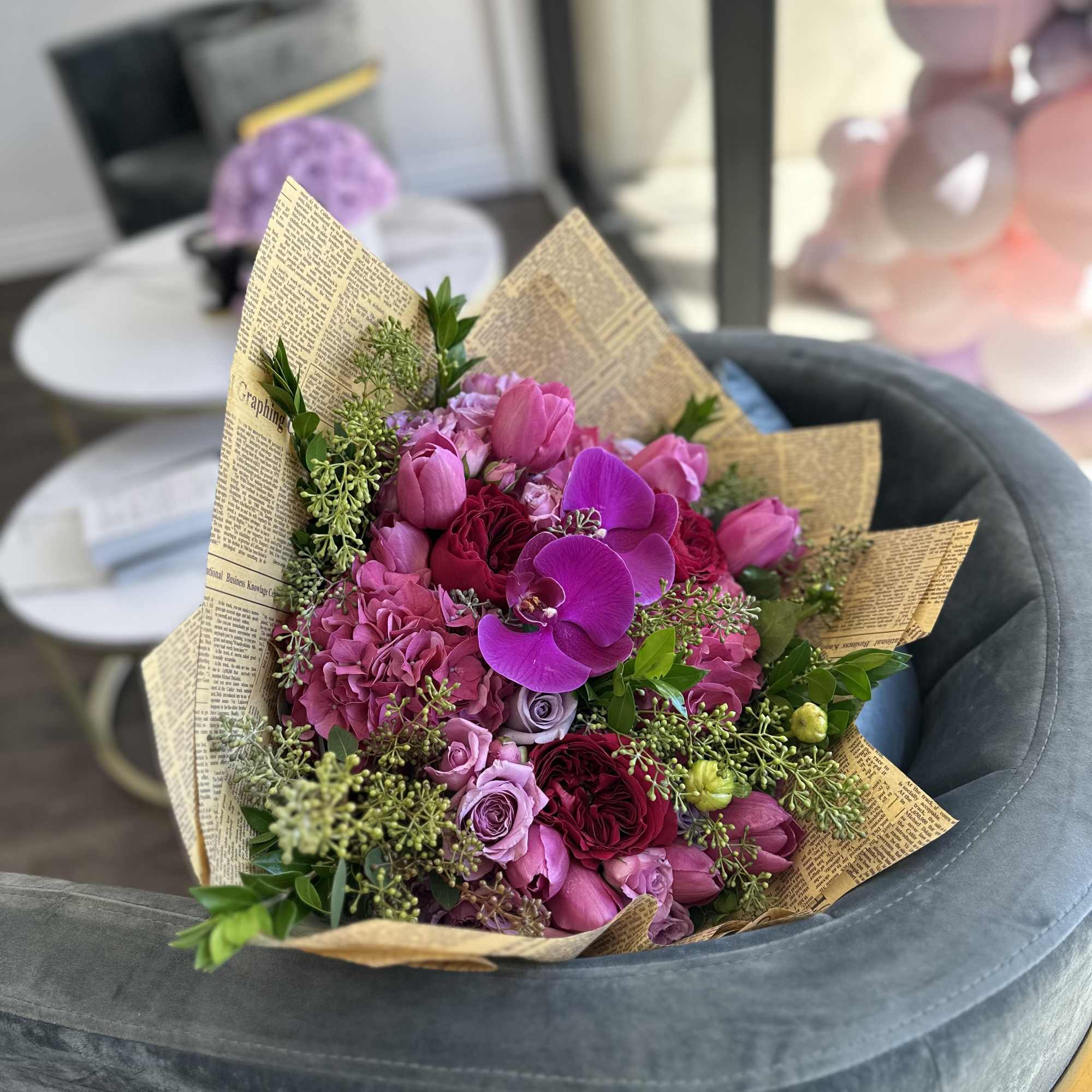 Pink and purple bouquet with roses and orchids wrapped in newspaper-style paper