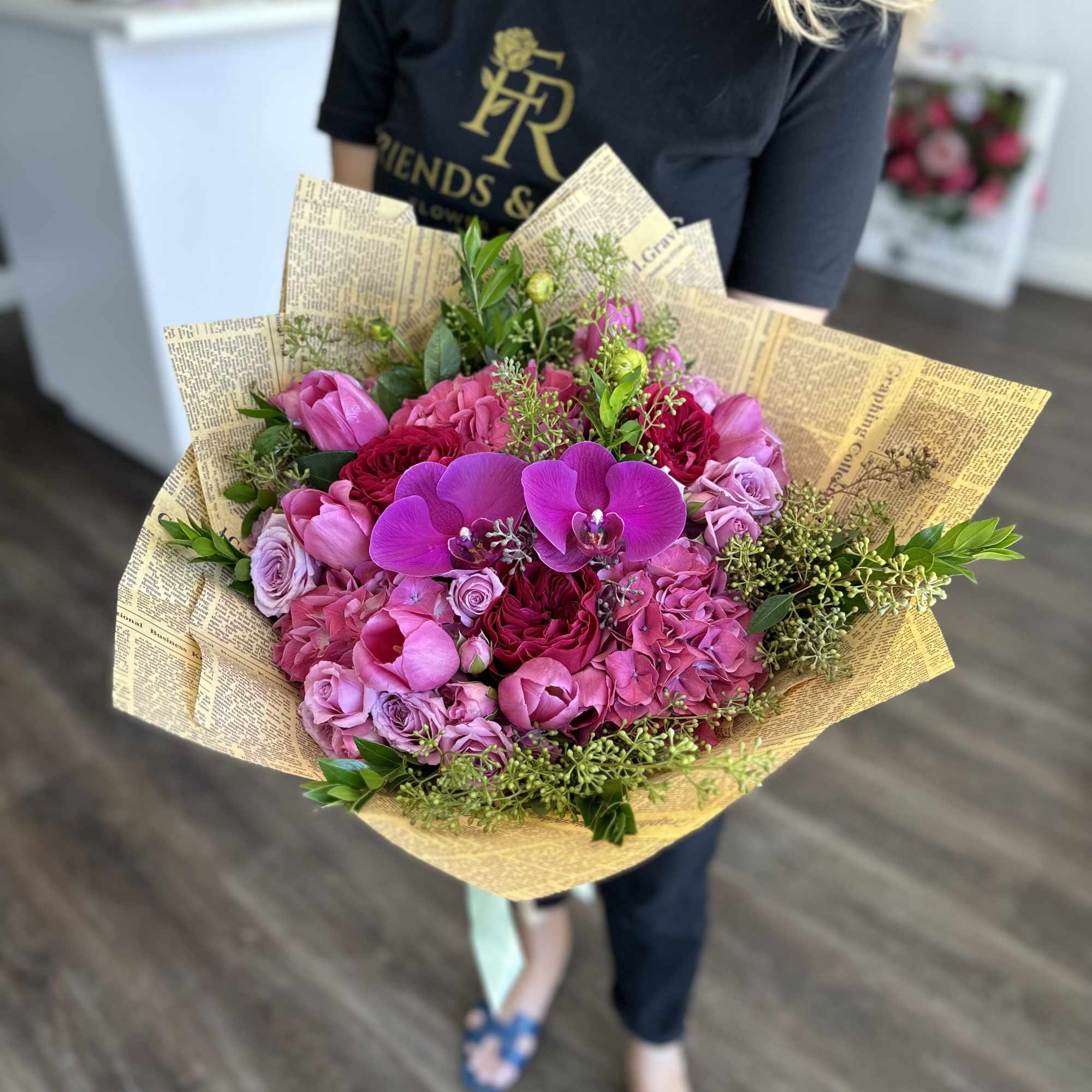 Pink and purple bouquet with orchids and roses wrapped in newspaper-style paper
