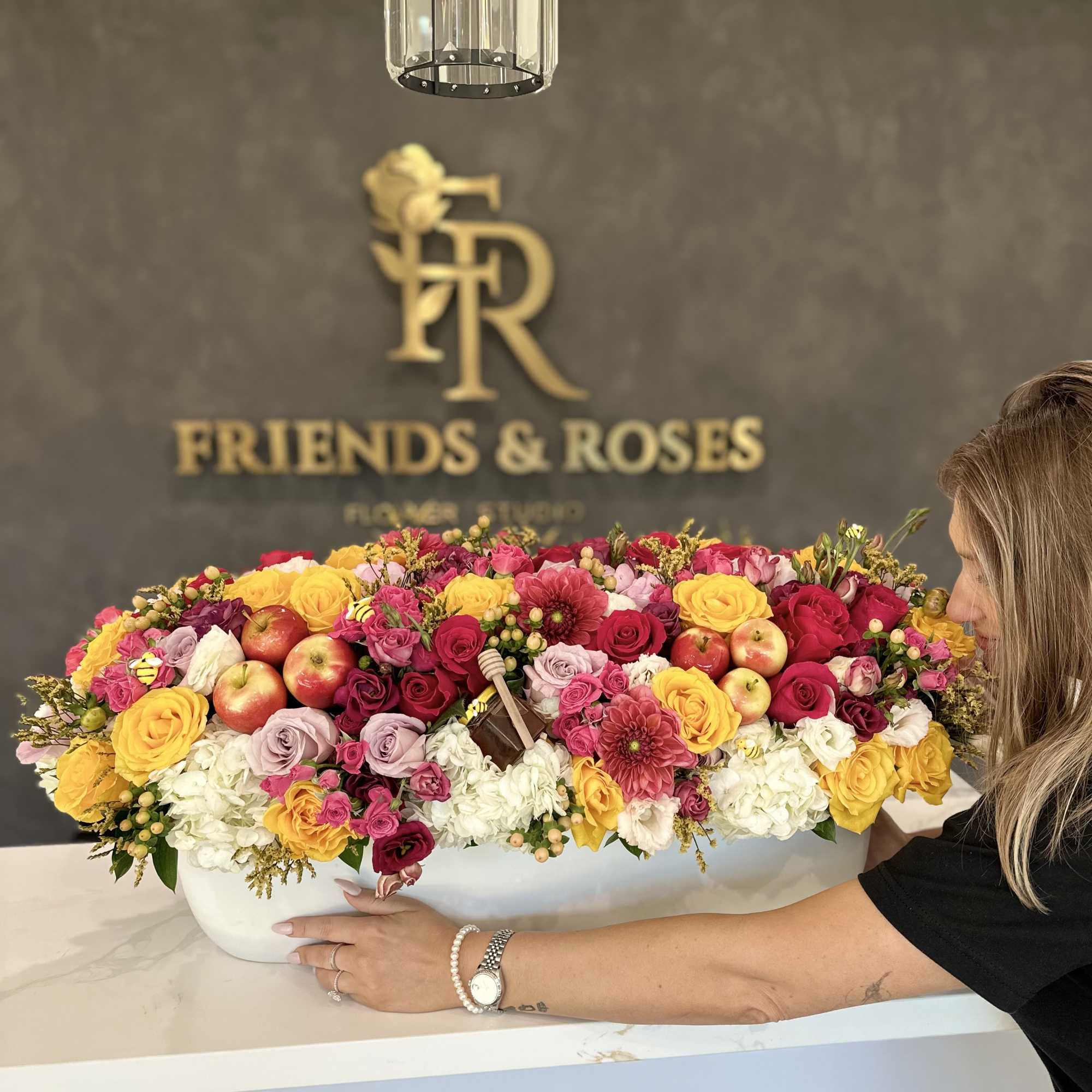 Large mixed flower arrangement in a white container with apples and honey jars
