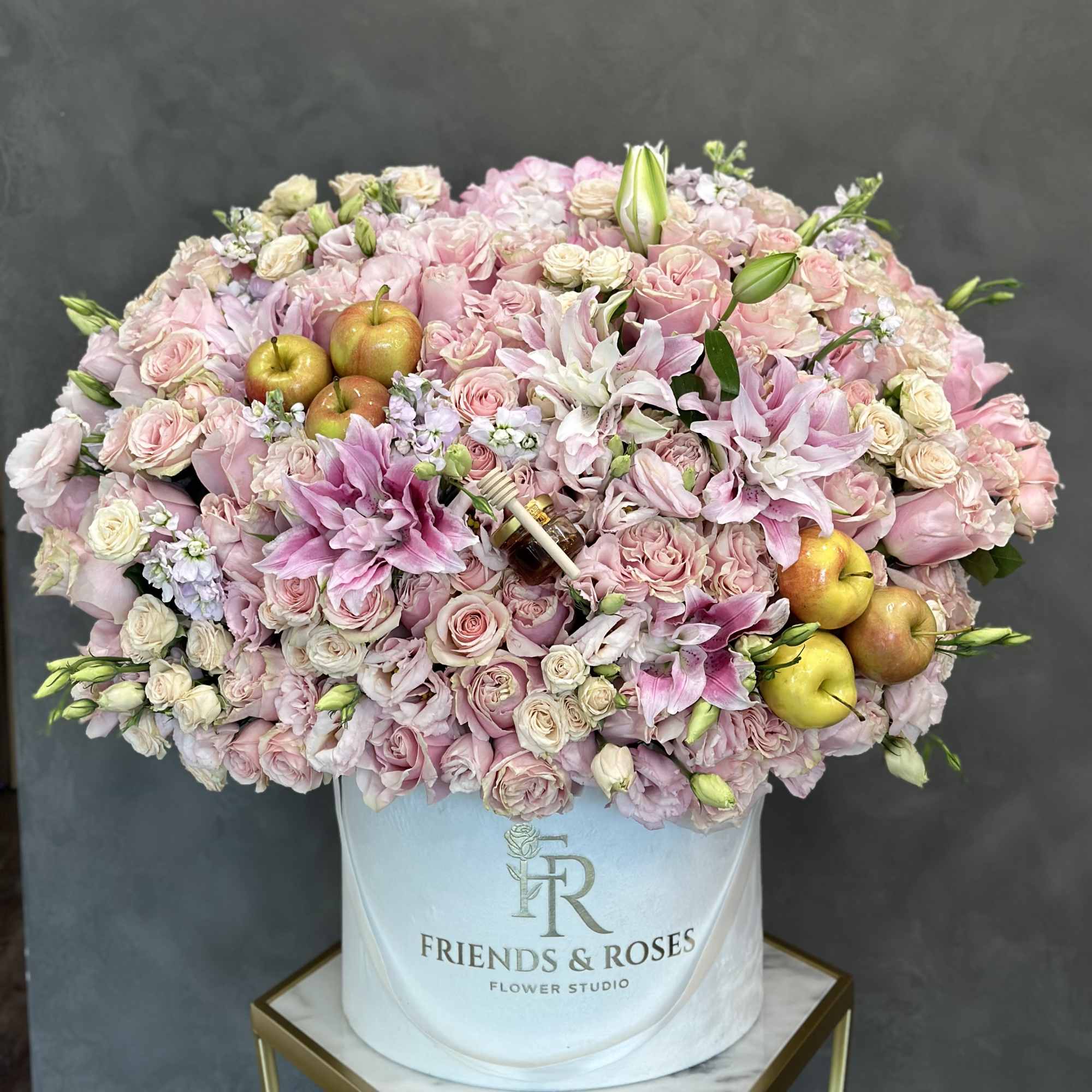 Large pink rose and lily arrangement in a white hat box with apples