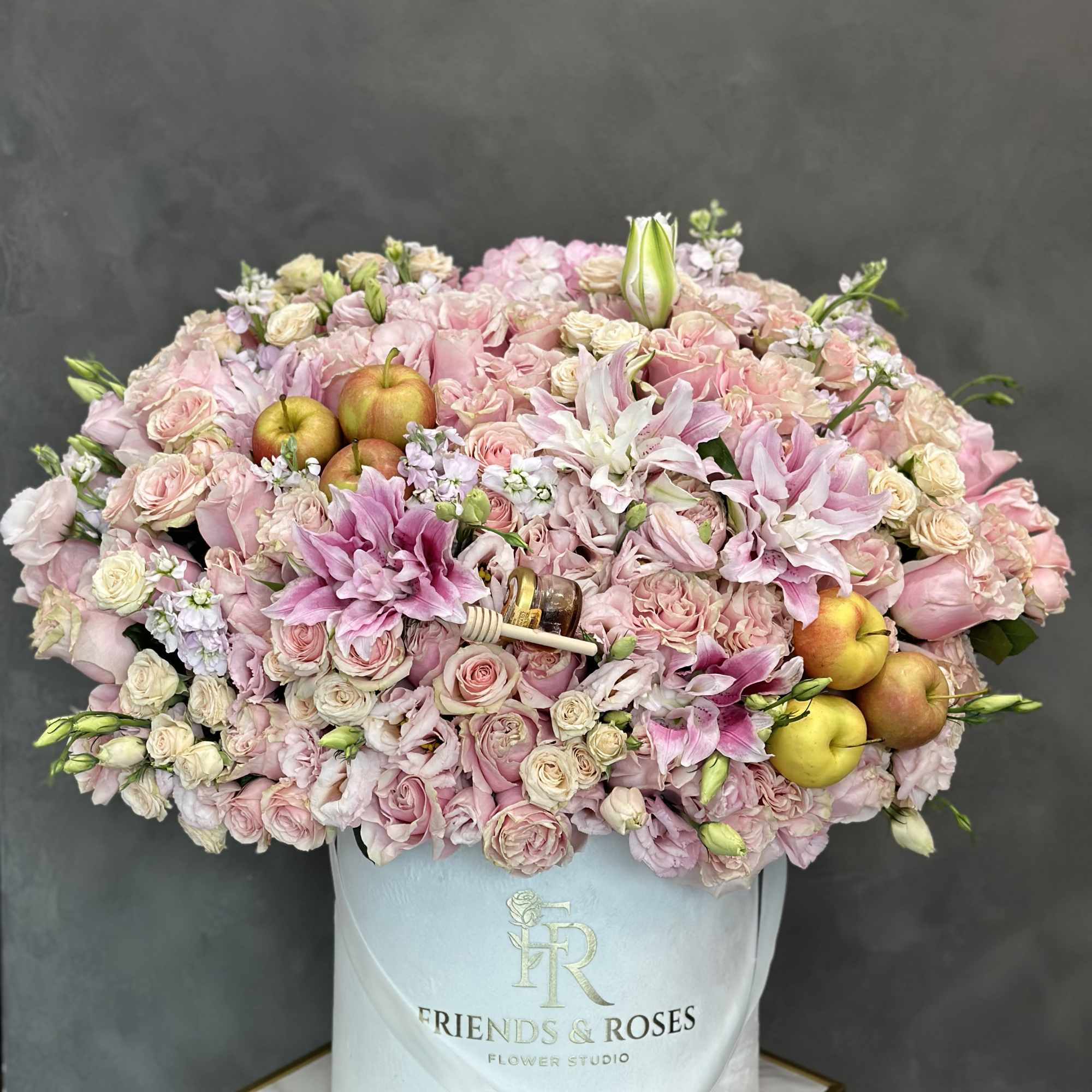 Pink roses and lilies arranged in a white hat box with apples and honey