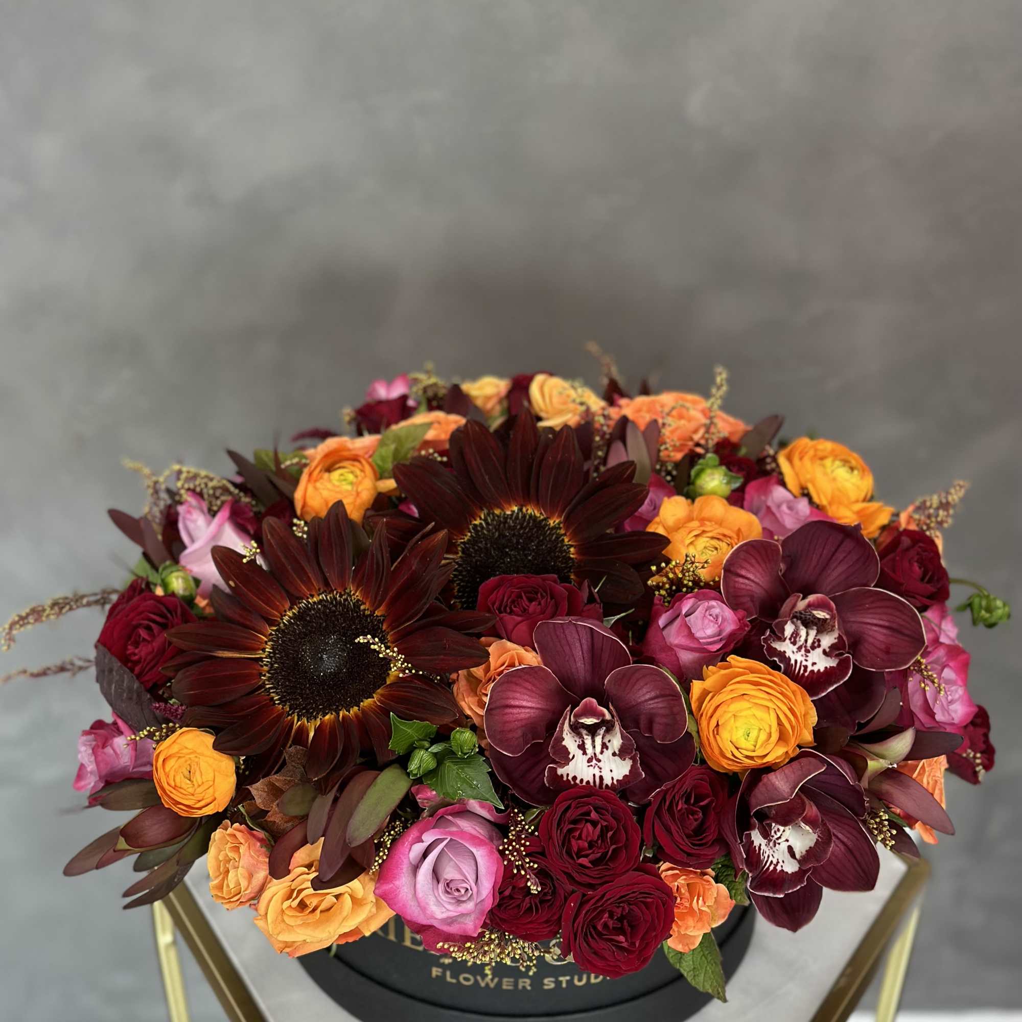 Round arrangement of burgundy, orange, pink, and red flowers in a black box