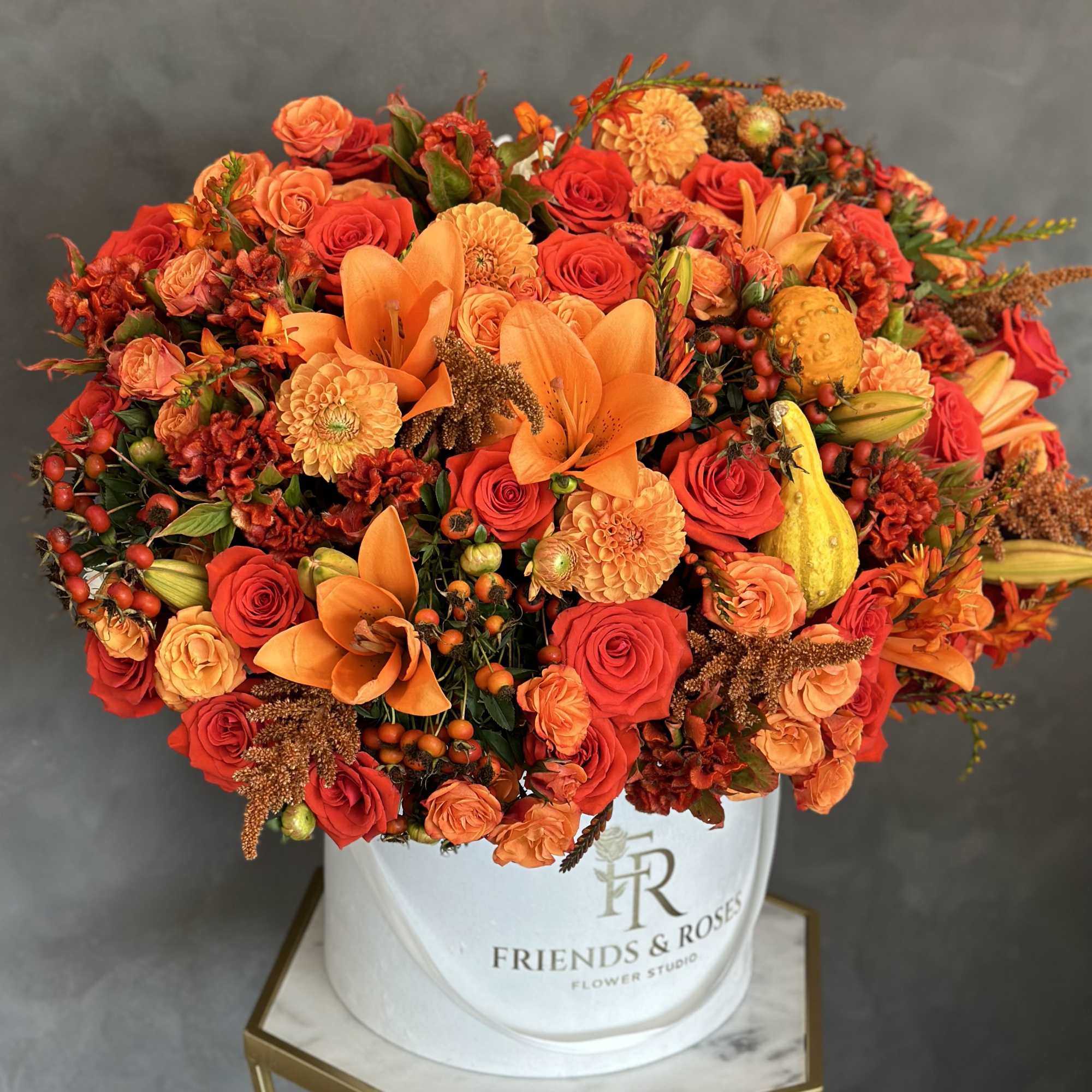 Orange and red floral arrangement in a white hat box
