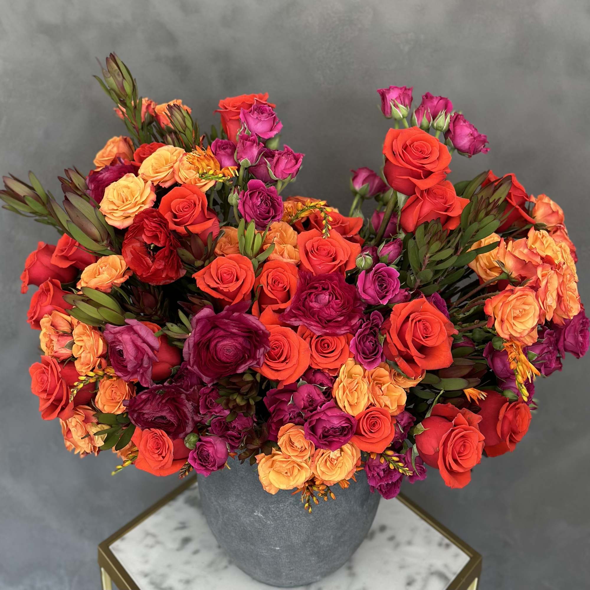 Mixed roses in red, orange, and magenta arranged in a gray vase