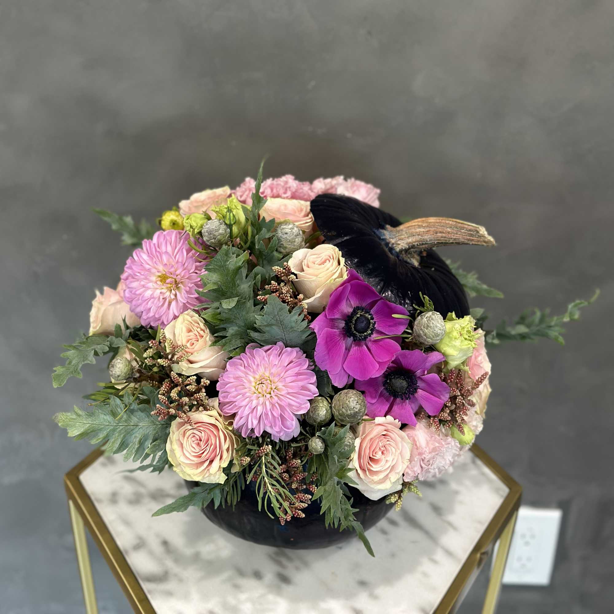 Mixed pink and cream flowers arranged in a black vase with a black feather accent