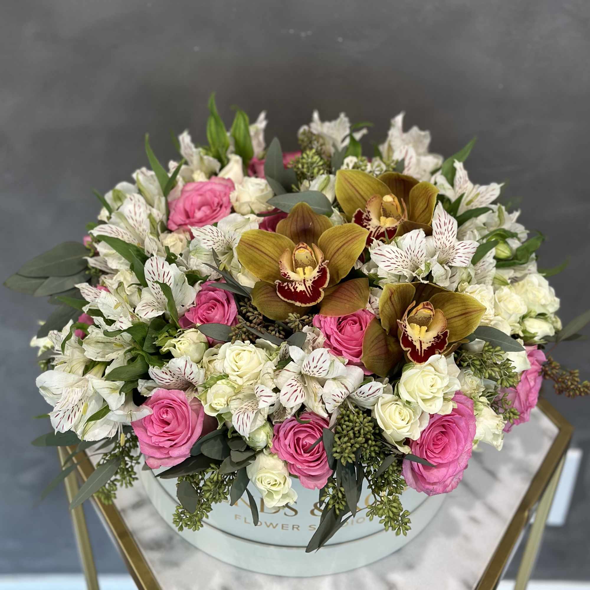 Round bouquet of pink and white roses with spotted white flowers in a box