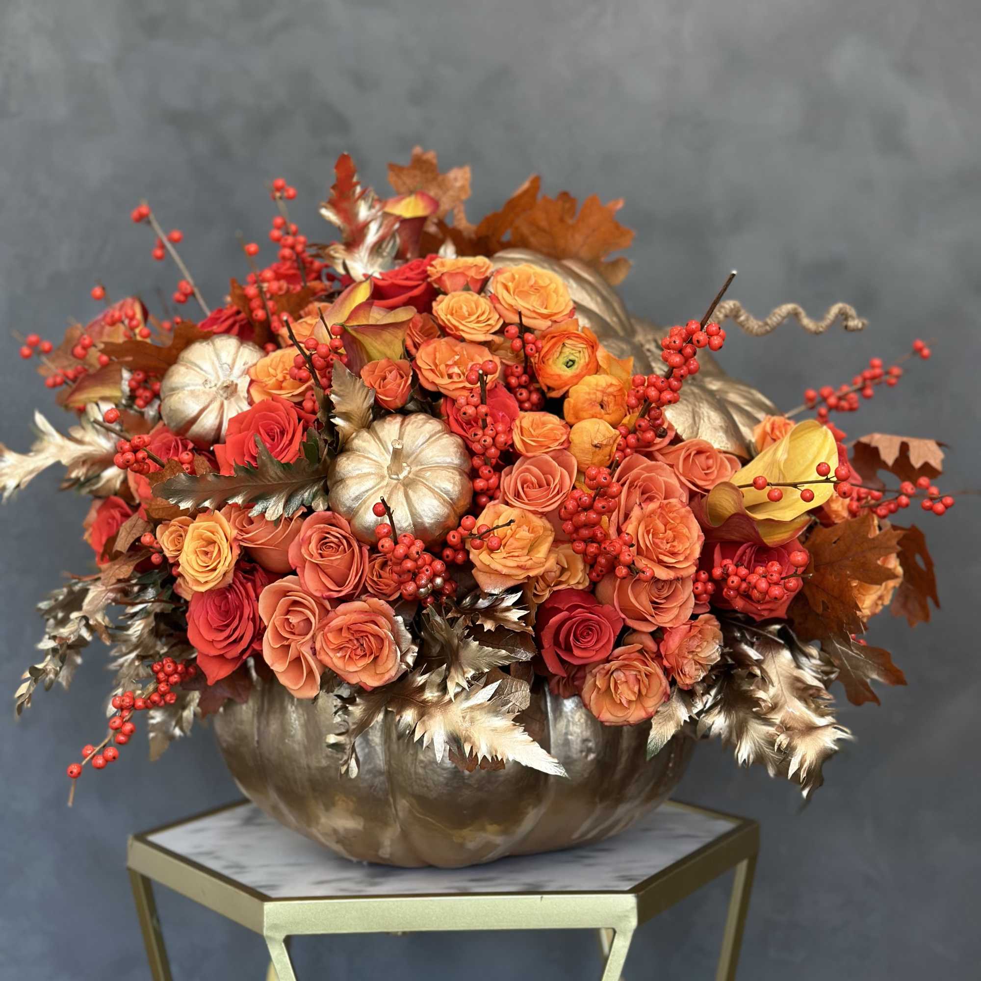 Orange and red rose arrangement in a metallic pumpkin container