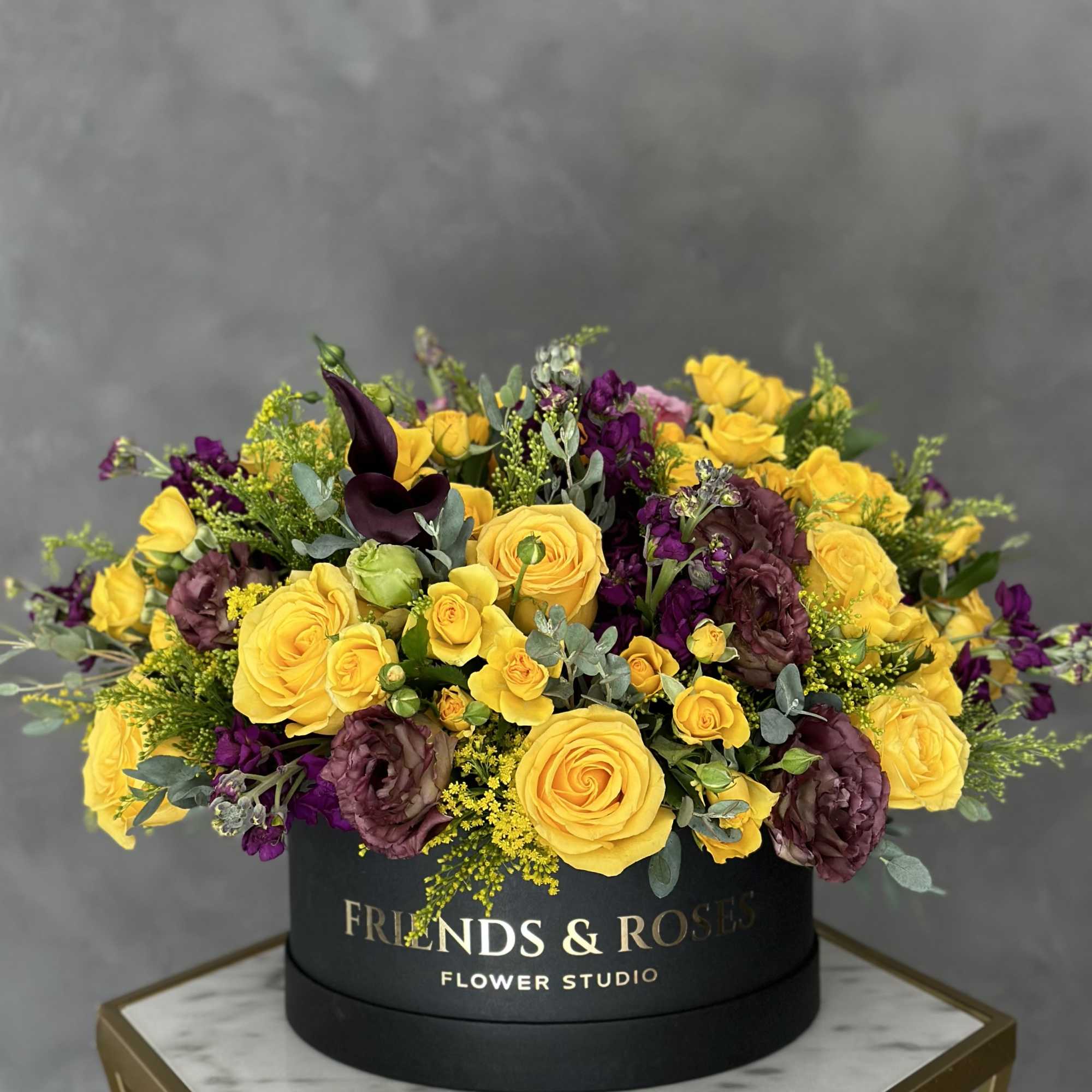 Yellow and purple roses arranged in a black round box