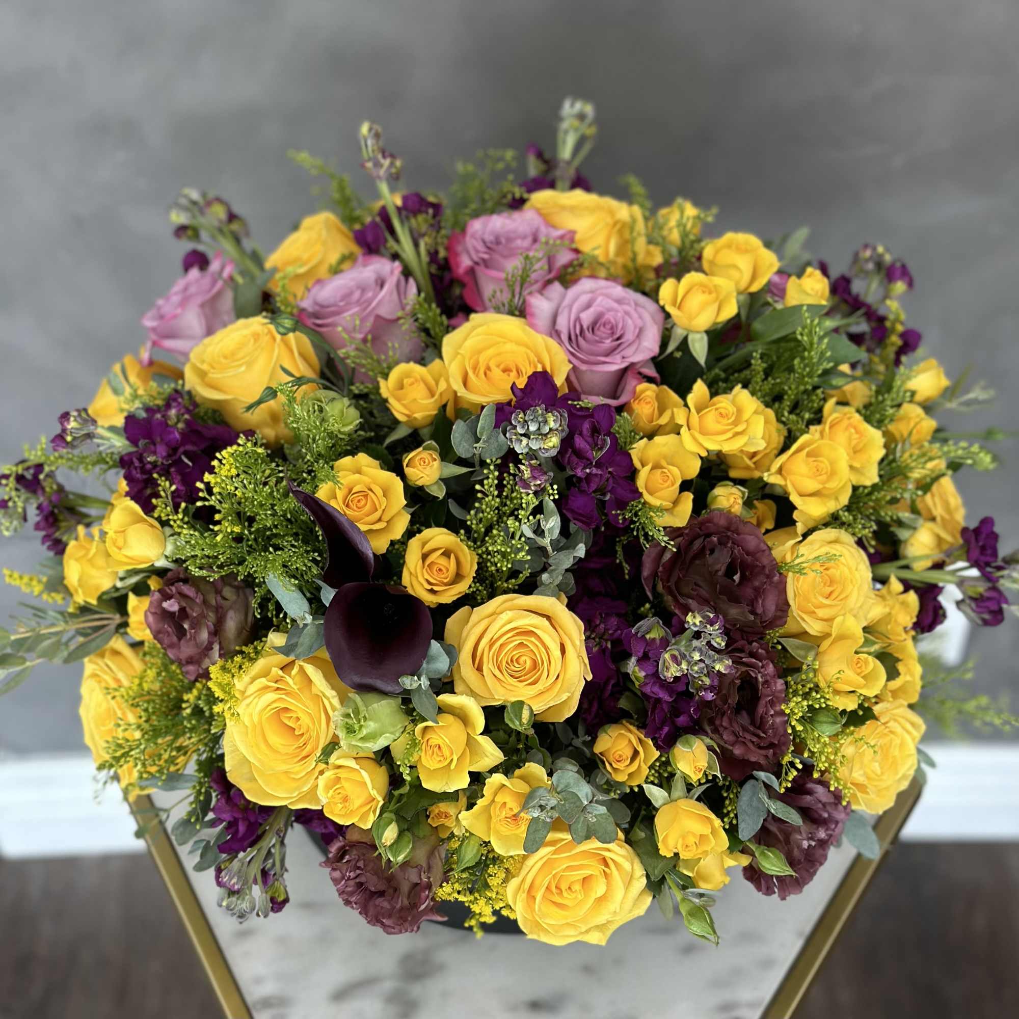 Bouquet of yellow and lavender roses with purple flowers in a vase