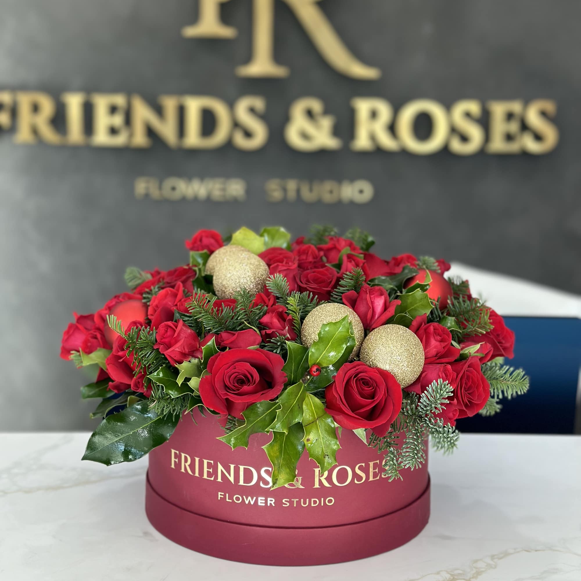 Red roses arranged in a round burgundy box with gold ornaments