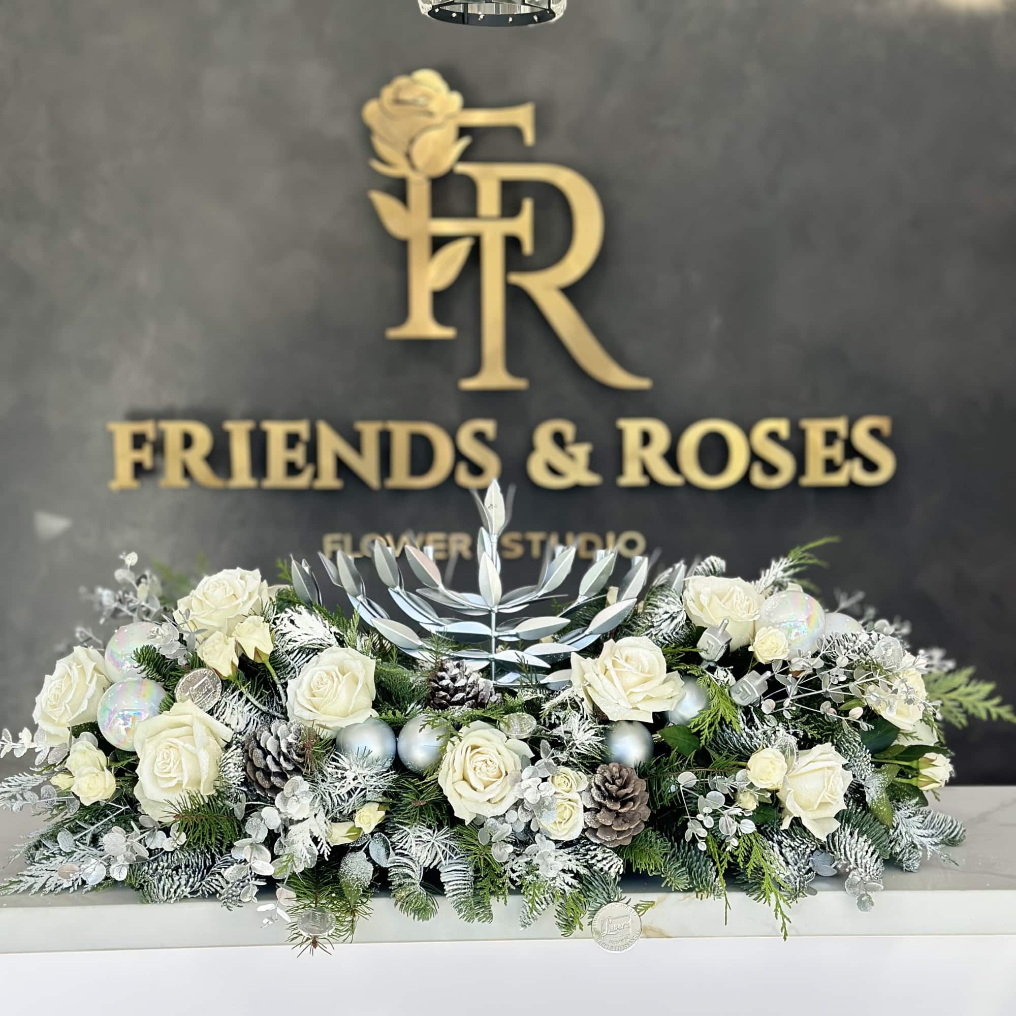 White roses arranged with frosted greenery and pinecones in a low centerpiece.