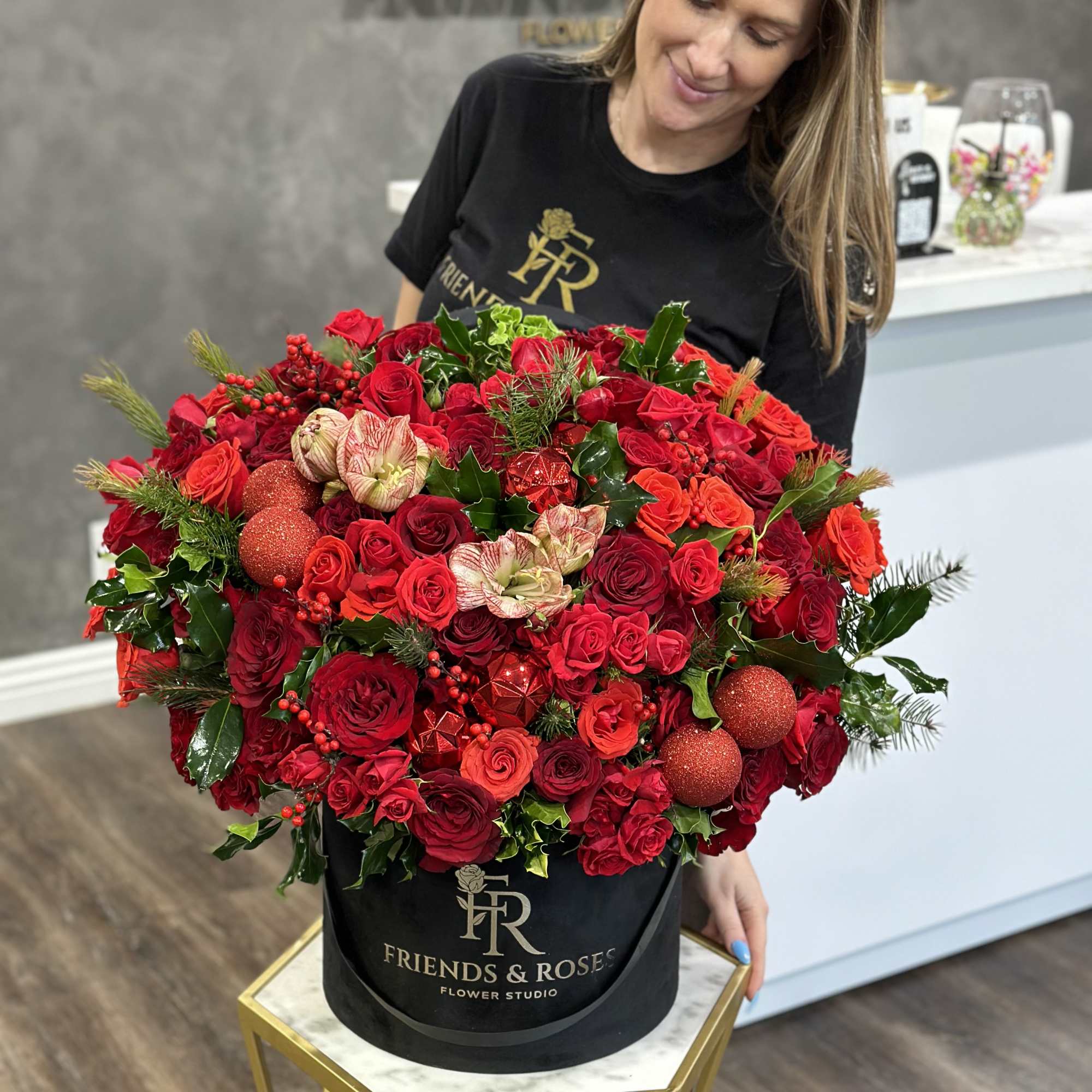 Large red rose arrangement in a black hatbox with holiday ornaments