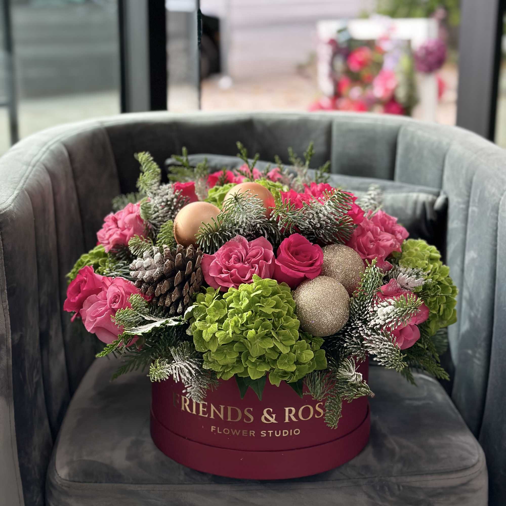 Pink roses and green hydrangeas arranged in a round box with ornaments and pinecones