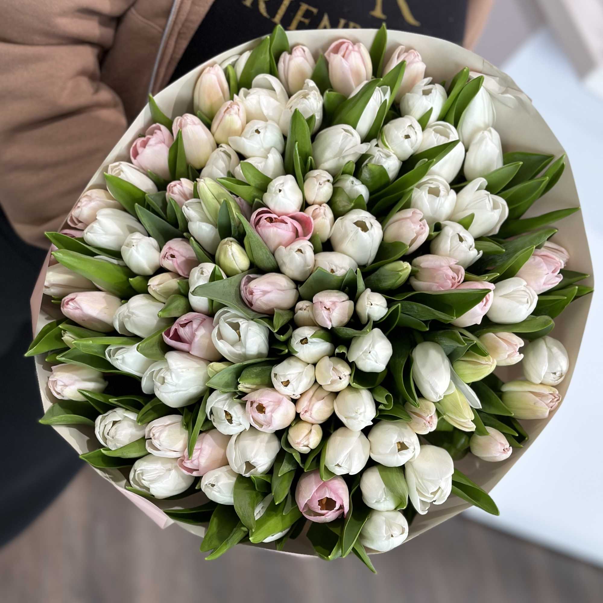 Round bouquet of white and pale pink tulips wrapped in paper