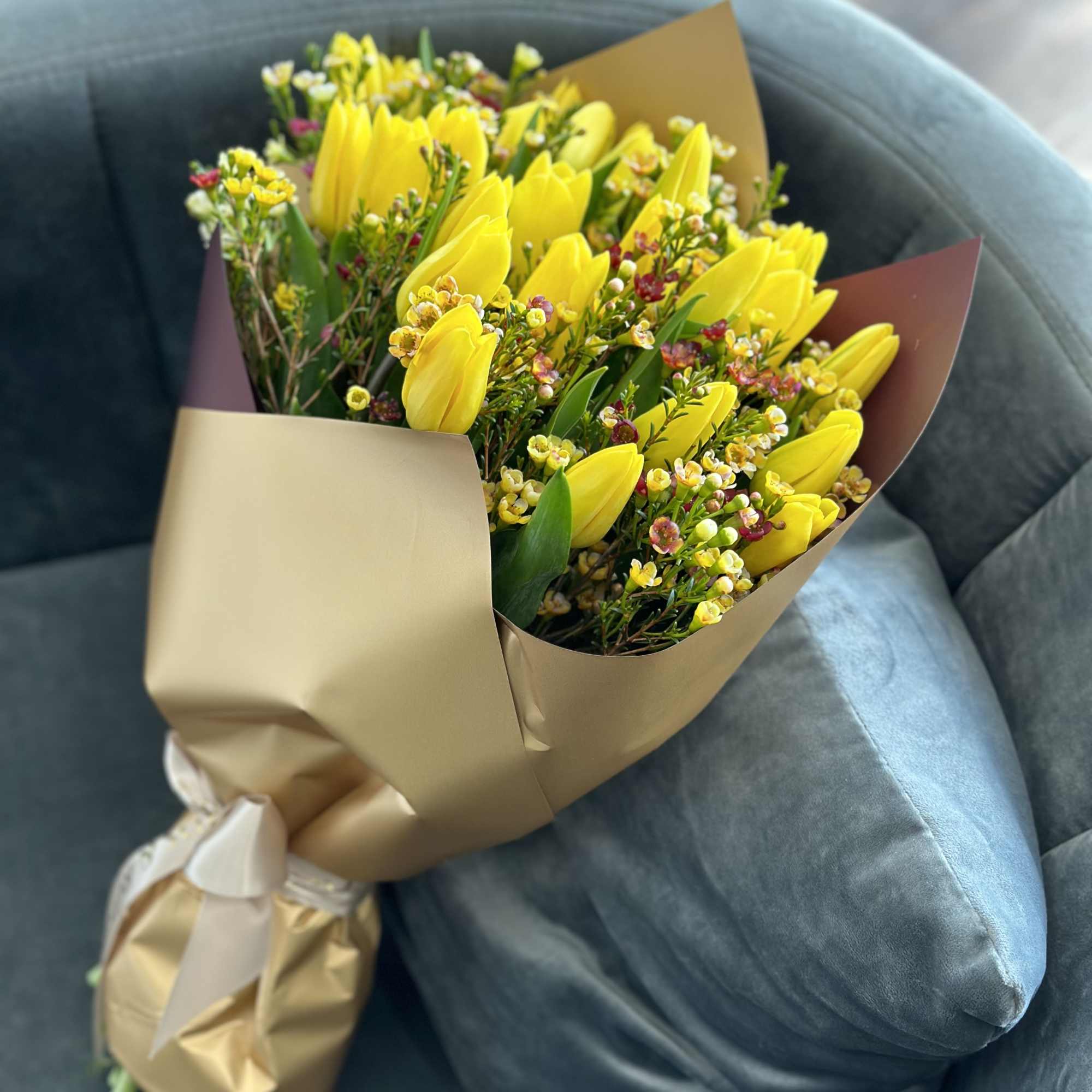 Bouquet of yellow tulips wrapped in tan paper with small filler flowers