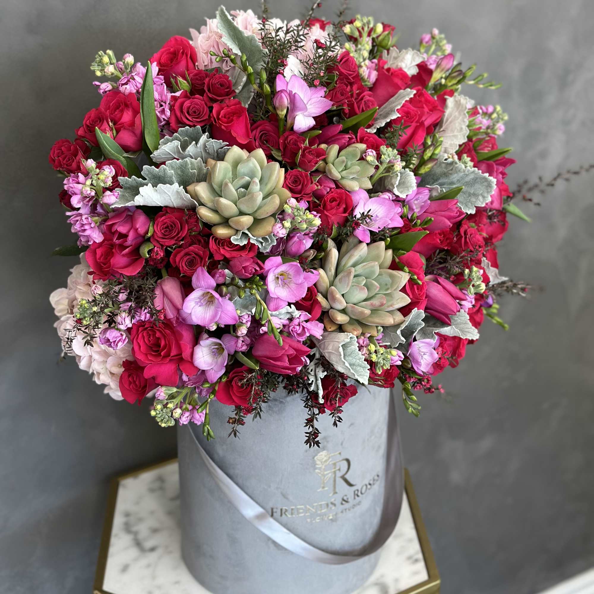 Pink and red roses with succulents in a gray hatbox
