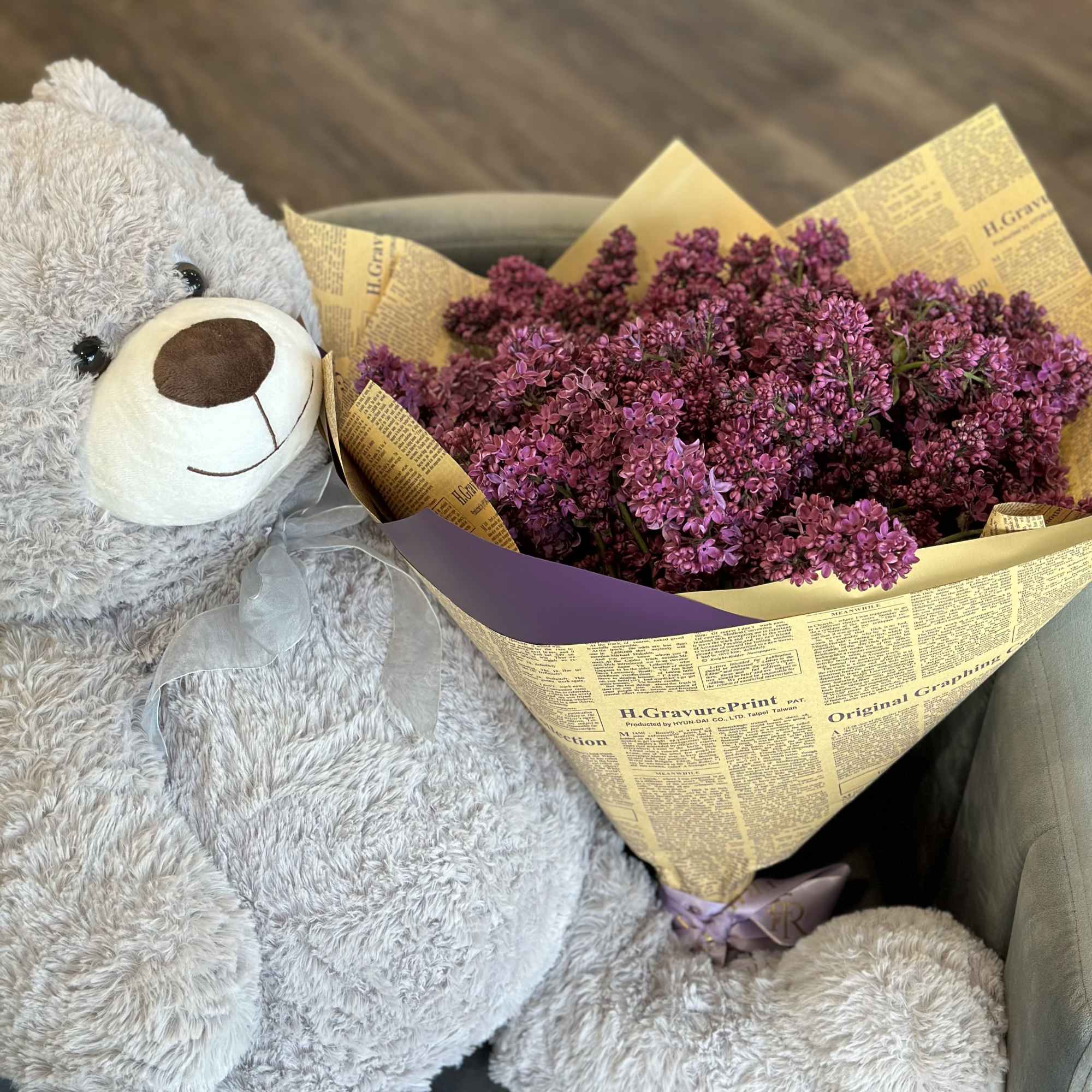 Purple lilac bouquet beside a large gray teddy bear