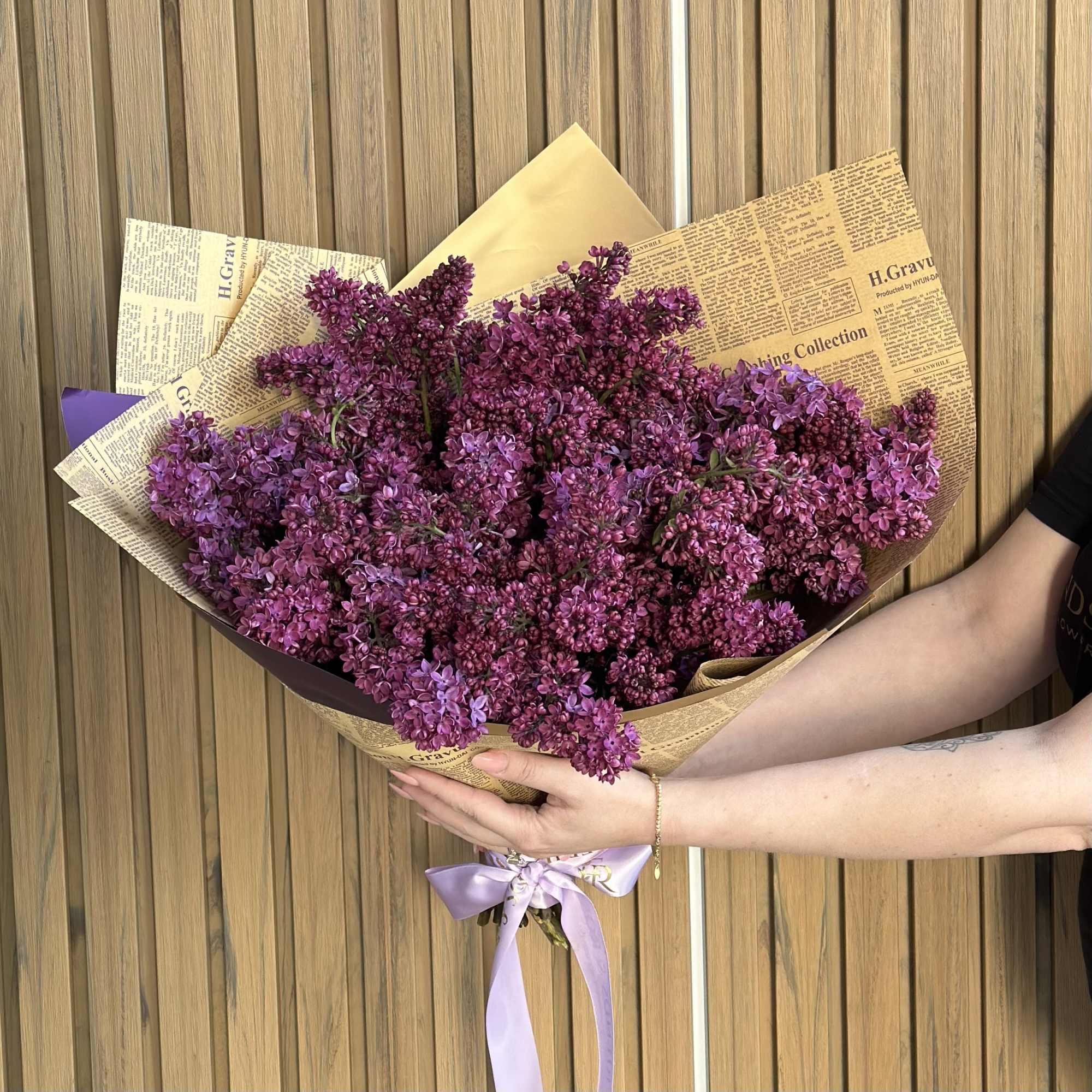 Bouquet of purple lilac flowers wrapped in newspaper-style paper with a lavender ribbon