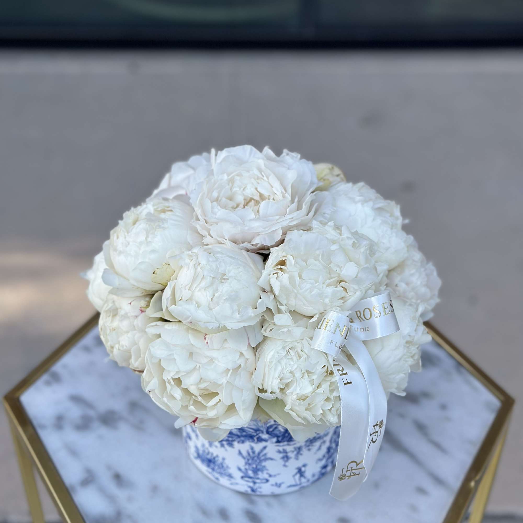 White peonies arranged in a blue-and-white ceramic box with a ribbon