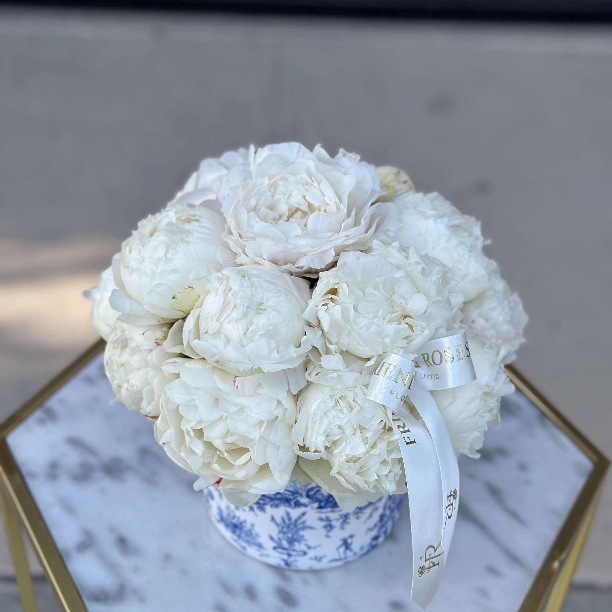 White peonies arranged in a blue-and-white porcelain box with a white ribbon