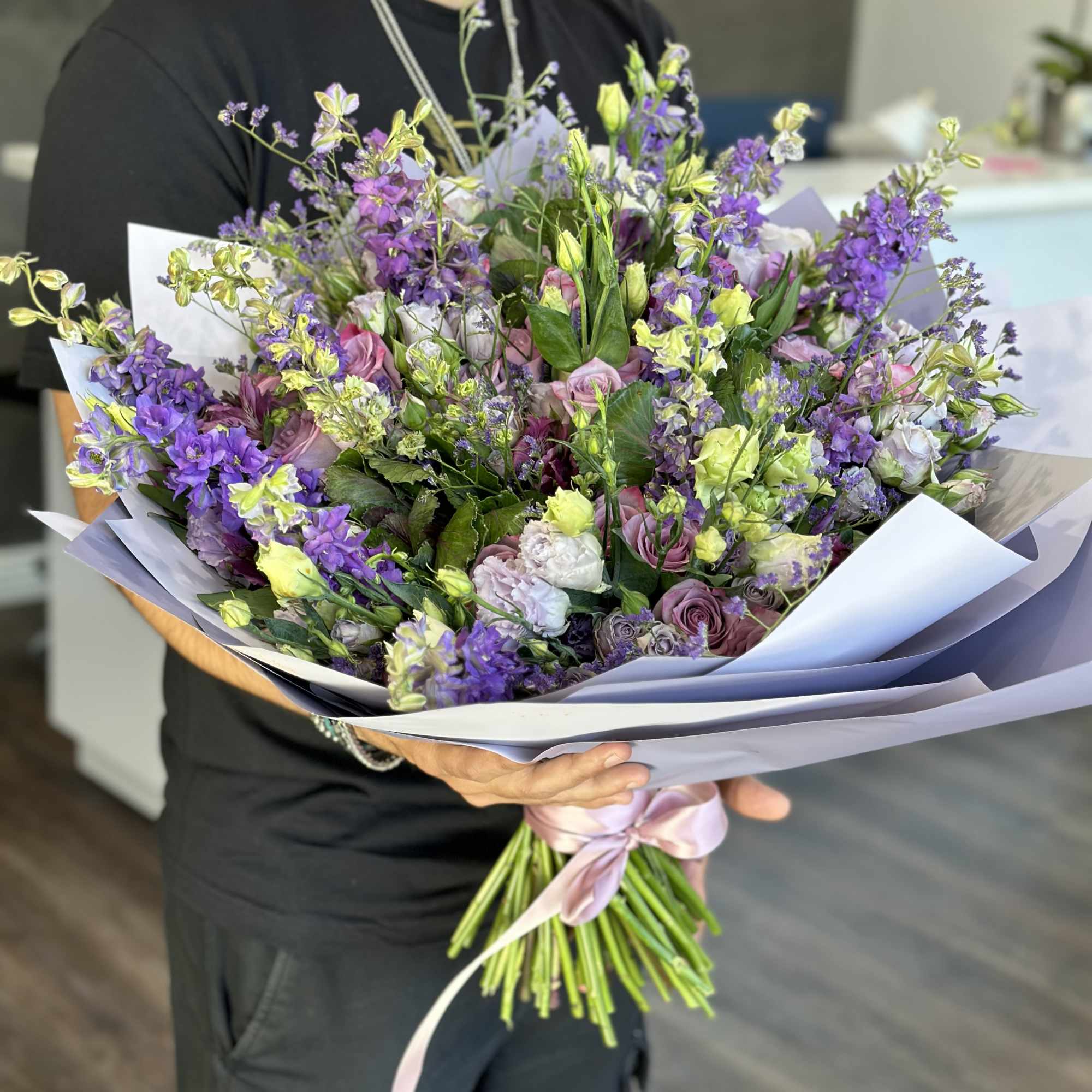 Large bouquet of purple and yellow flowers wrapped in pale paper