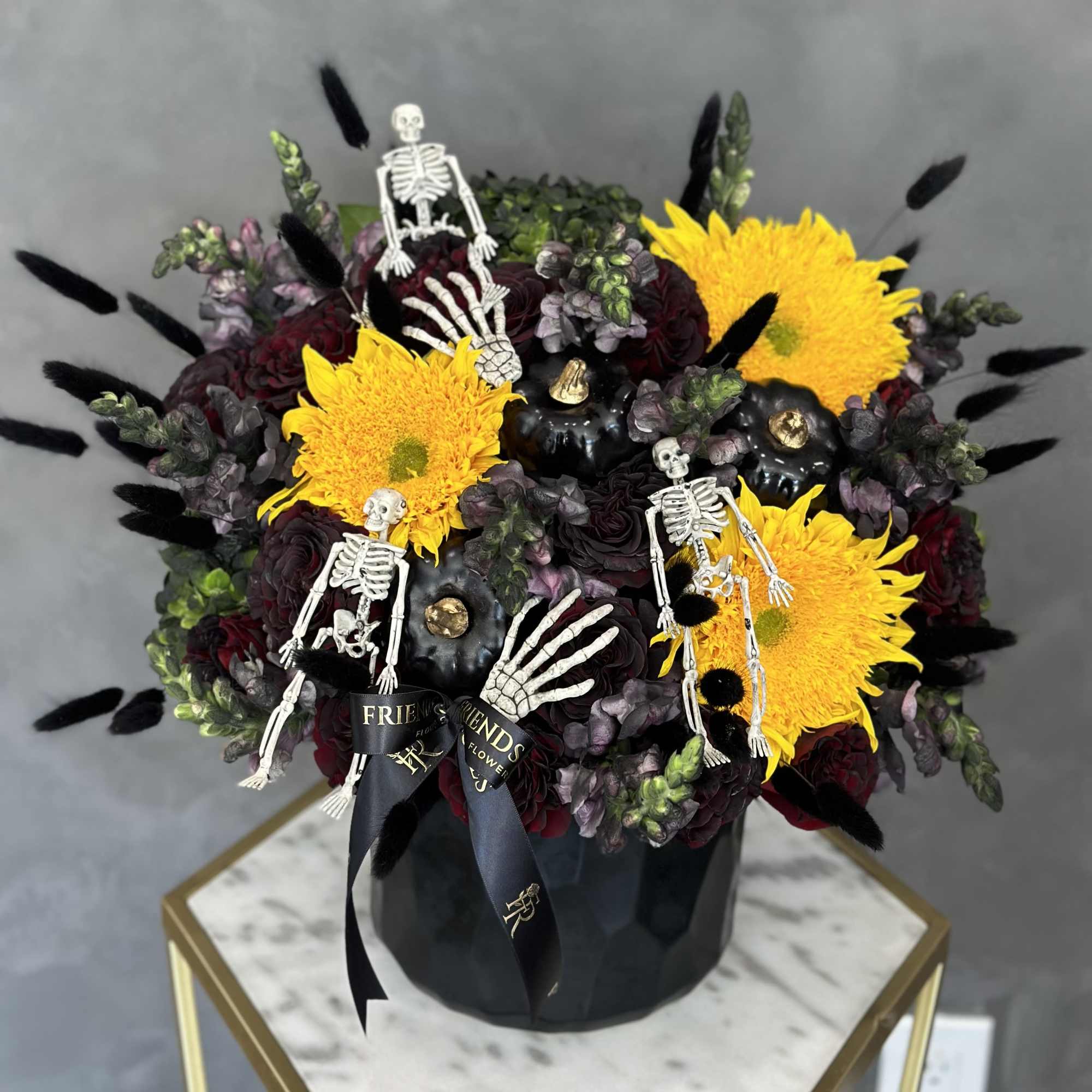 Halloween bouquet with yellow mums, dark roses, and skeleton decorations in a black box