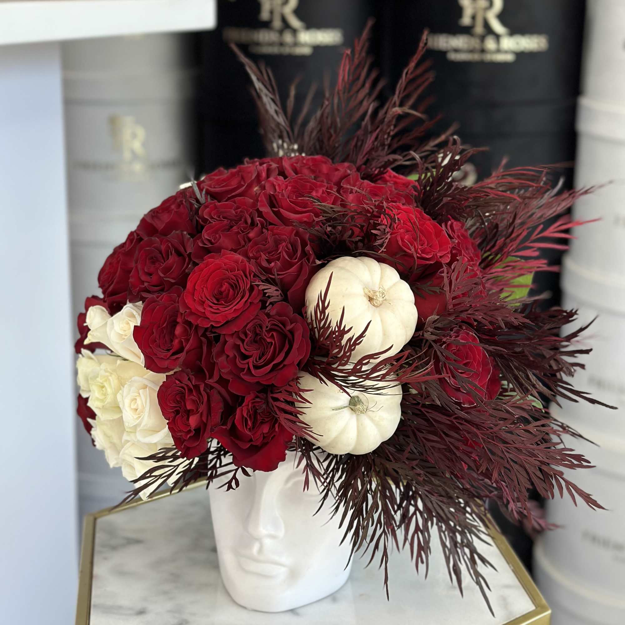 Red and white roses arranged in a white face-shaped vase with burgundy foliage