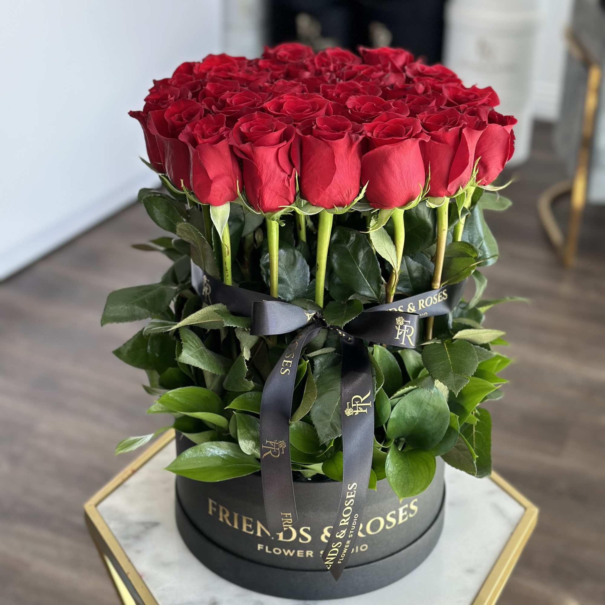 Round box of red roses with a black ribbon and green foliage