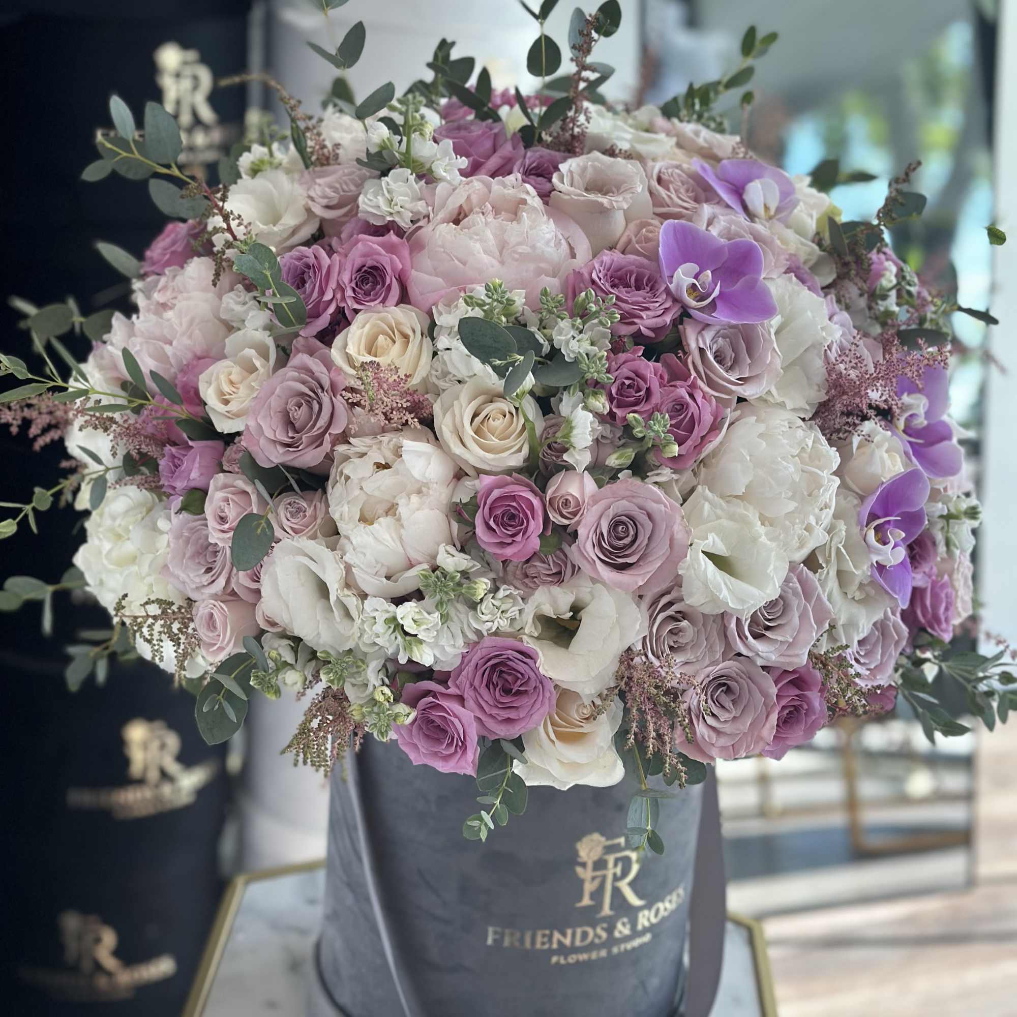 Large pastel bouquet of roses and orchids in a gray hat box