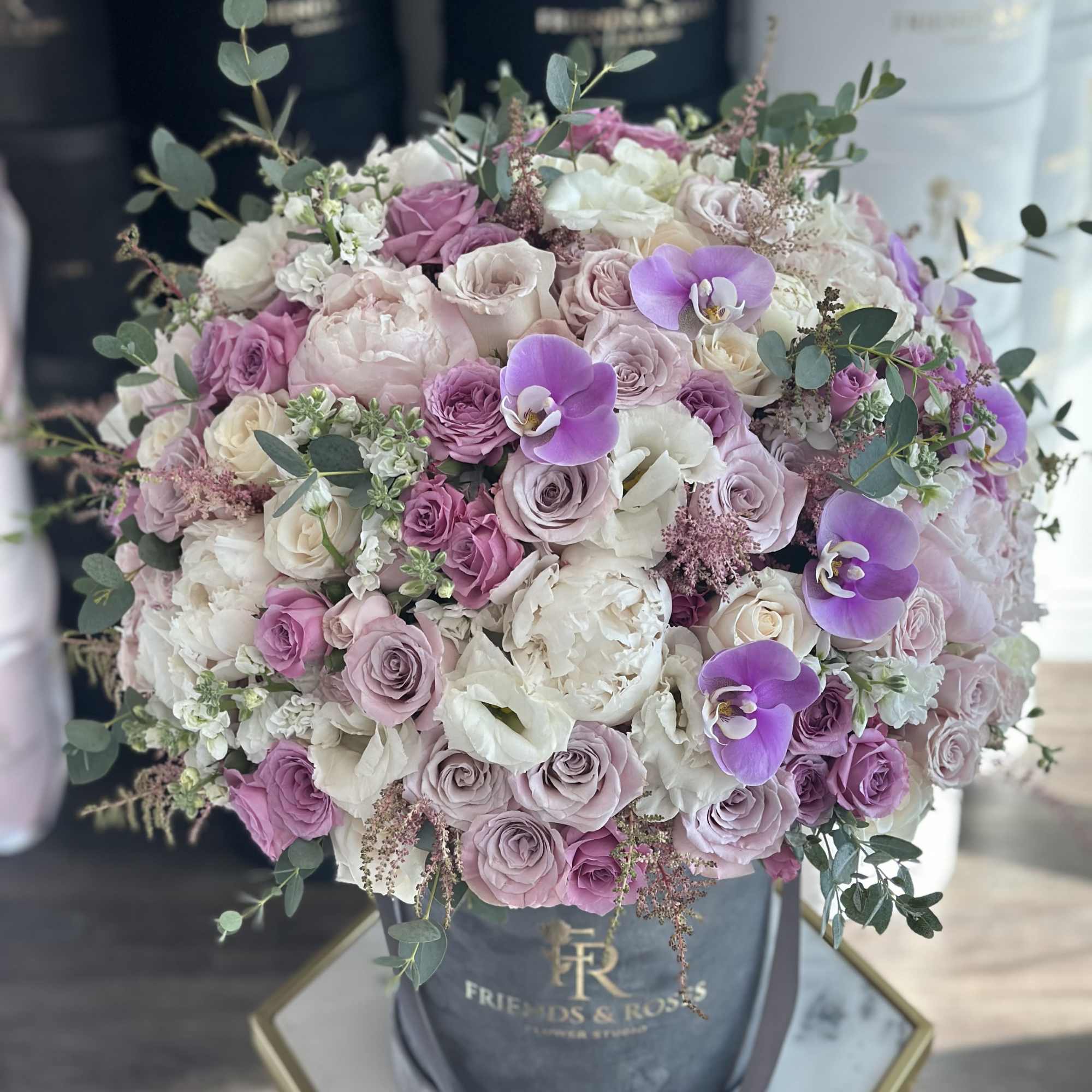 Round bouquet of pink and white roses with purple orchids in a hatbox